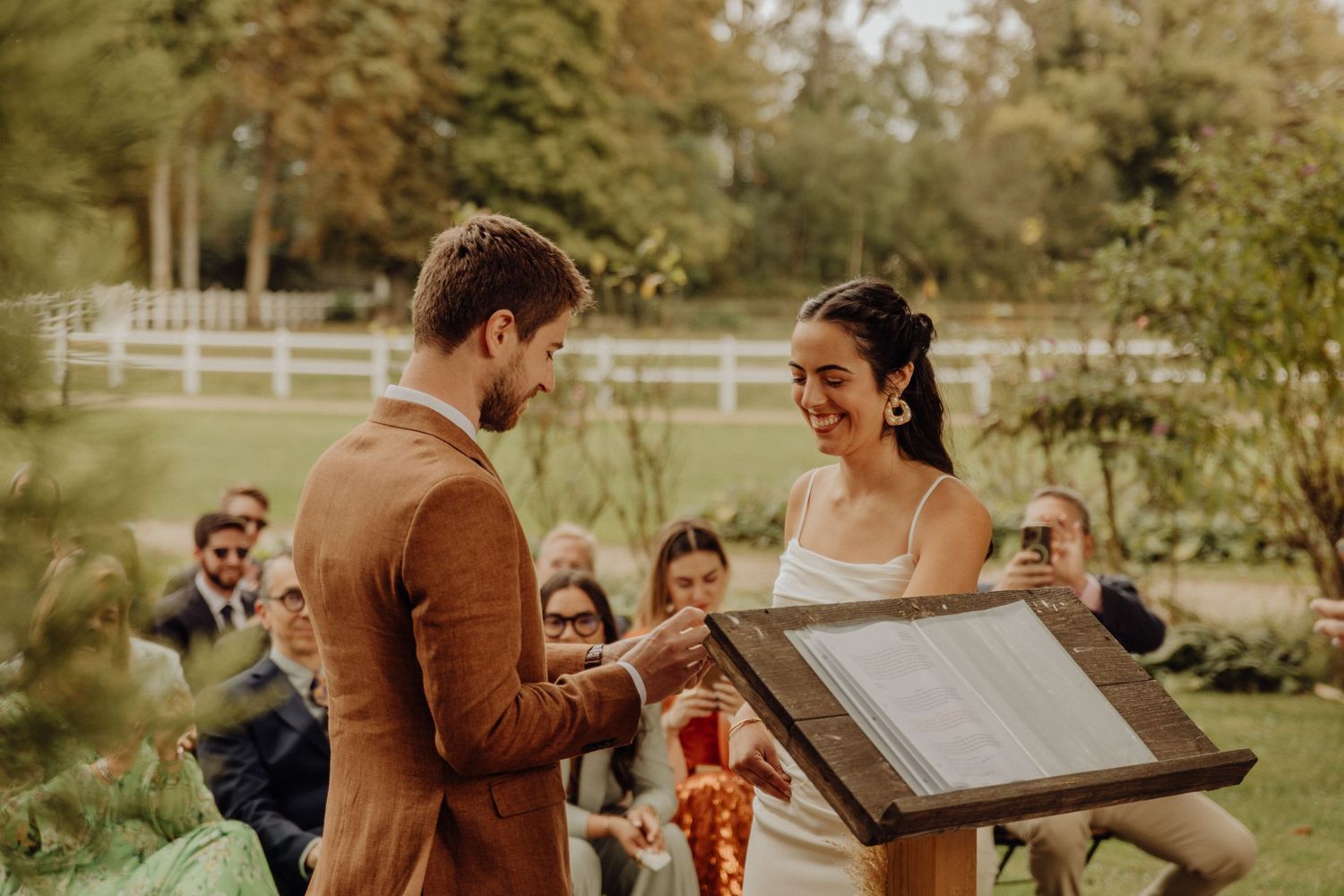 A couple shares an intimate moment during their outdoor autumn wedding ceremony in a garden setting.
