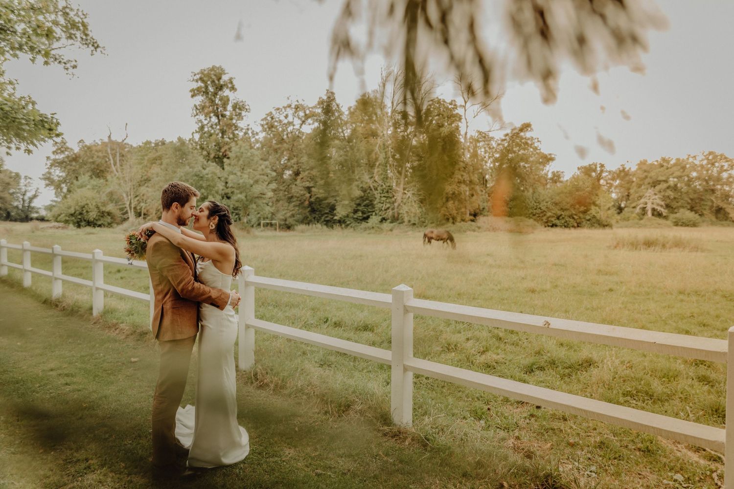 A romantic outdoor wedding photoshoot in a rustic setting with white fencing and golden sunlight.