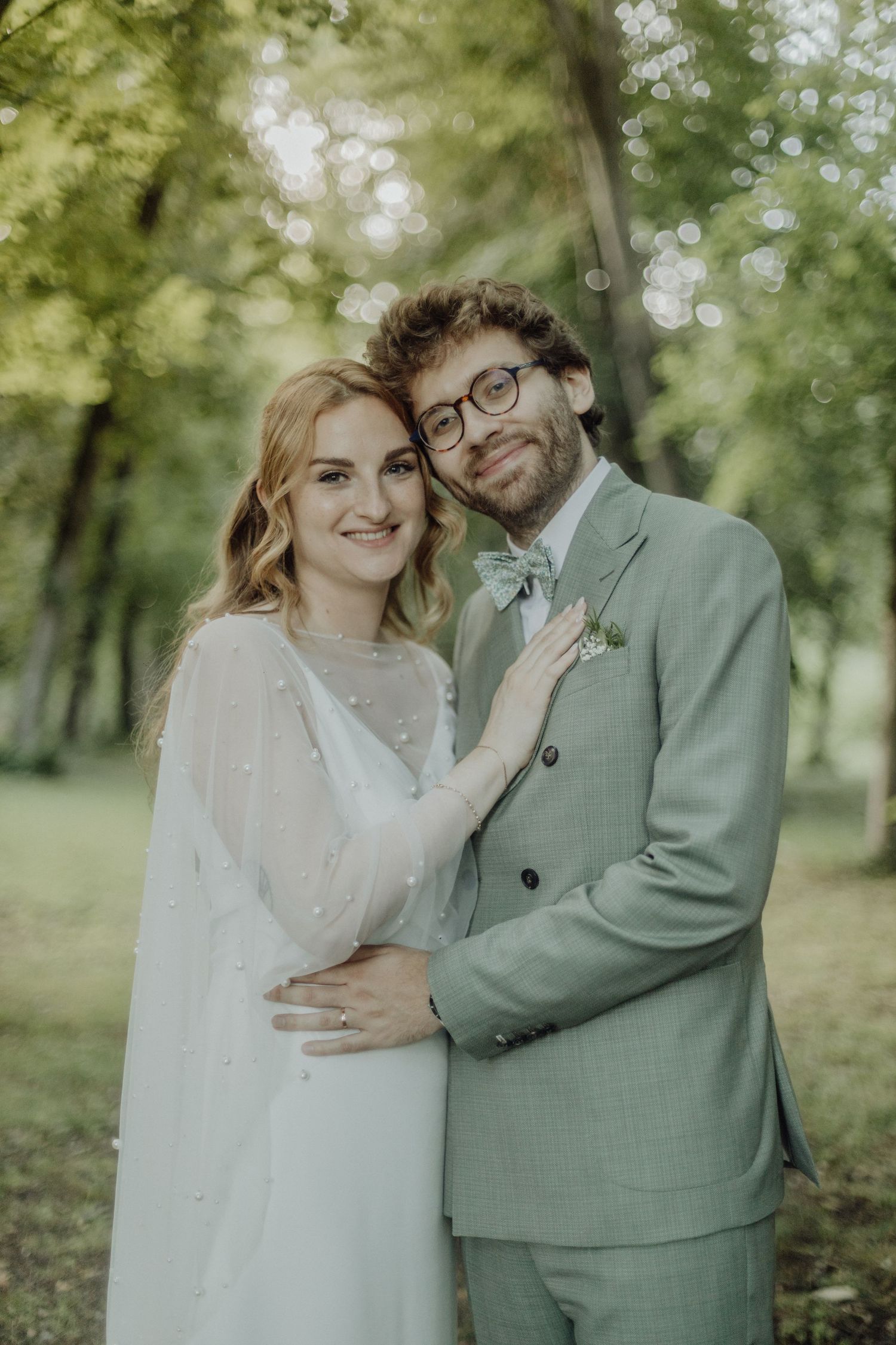 A couple shares intimate moments in a lush green outdoor setting wearing elegant wedding attire.