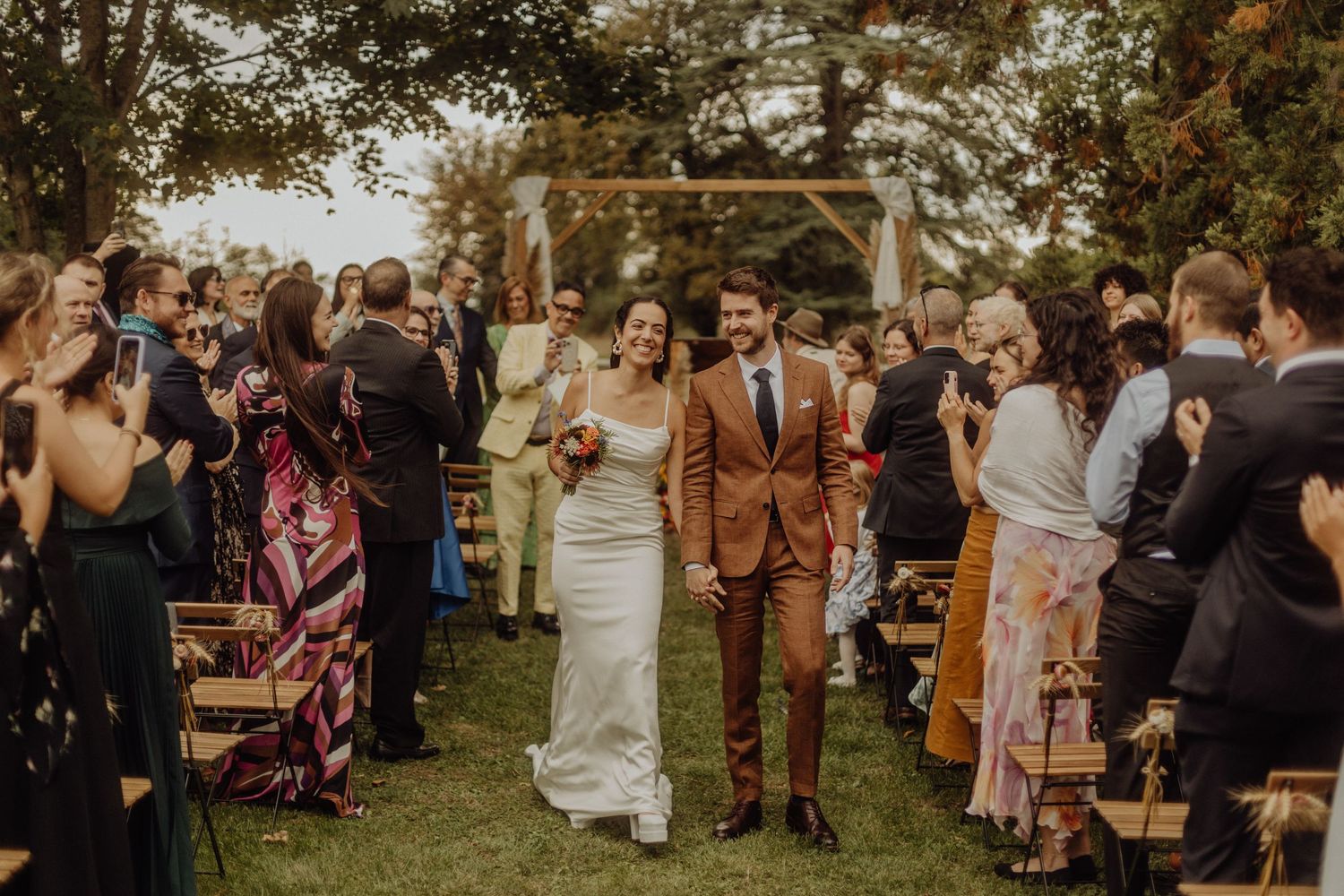 Wedding guests gather outdoors in a garden setting during a casual ceremony celebration.