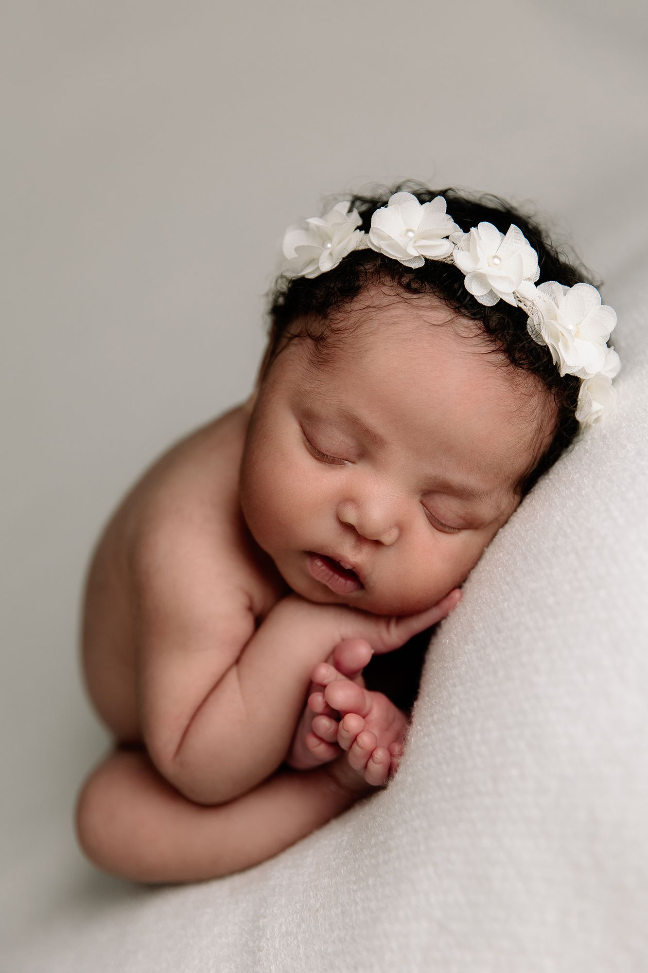 newborn girl curled up and sleeping on white blanket, wearing floral headband