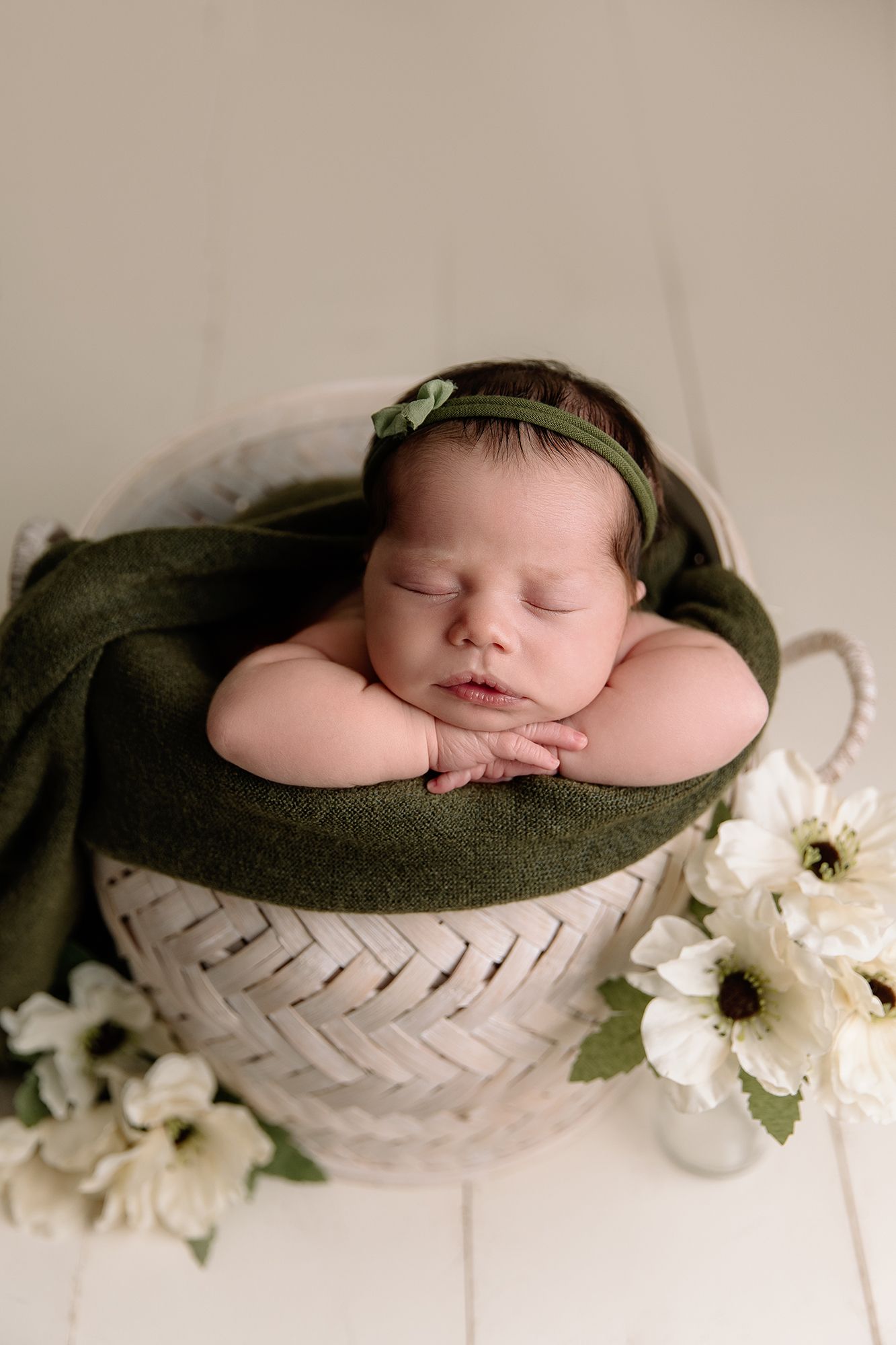 baby girl posed in white basket with green blanket surrounded by flowers