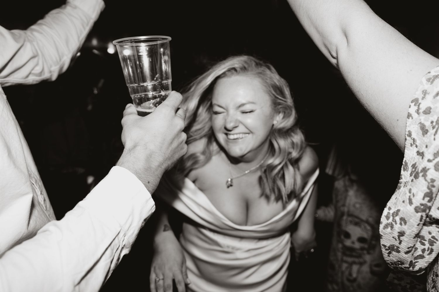 A candid black and white photograph shows wild party scene with raised glasses in celebration.
