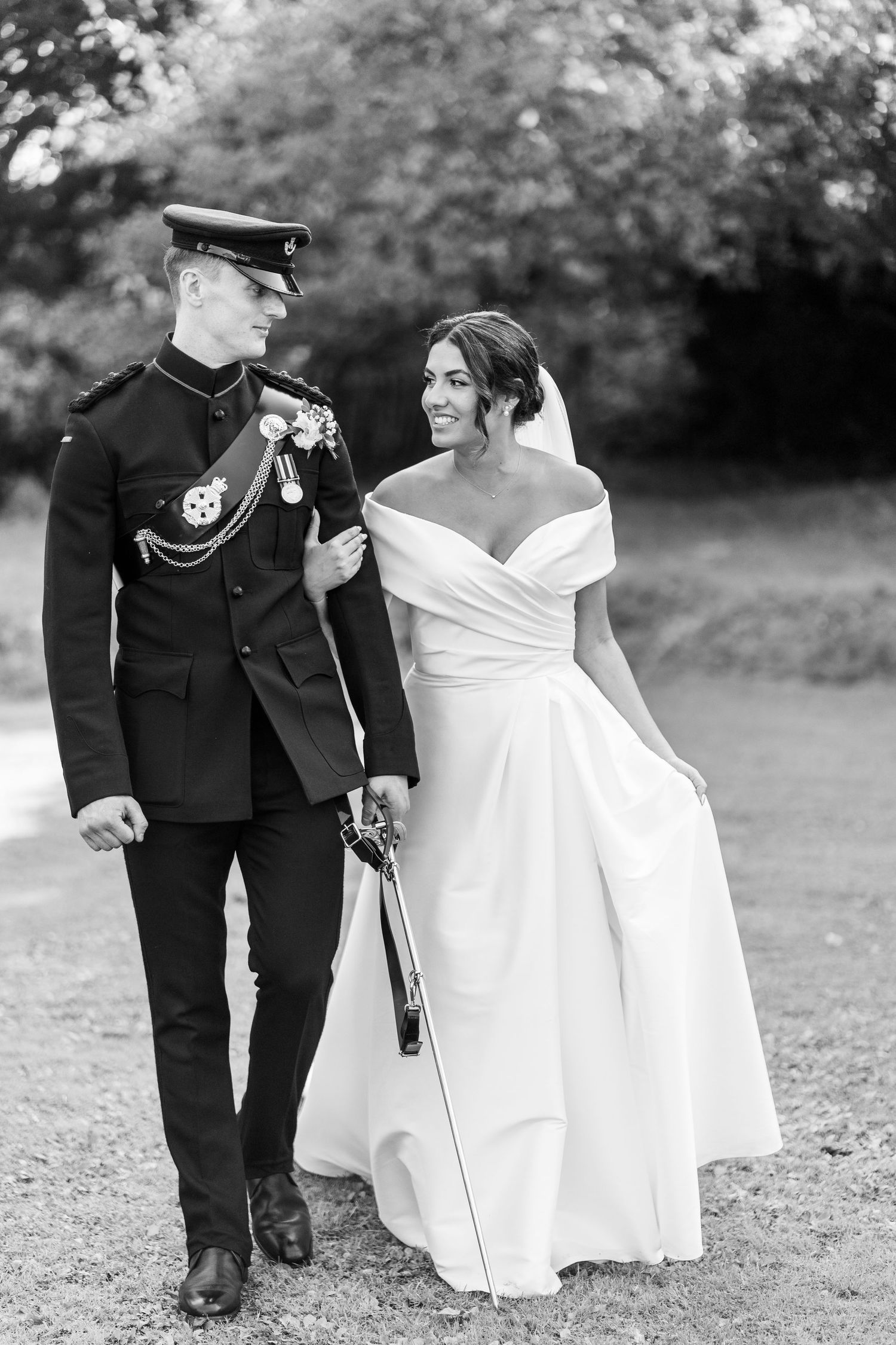 Black and white wedding photo of couple walking outdoors in formal attire.