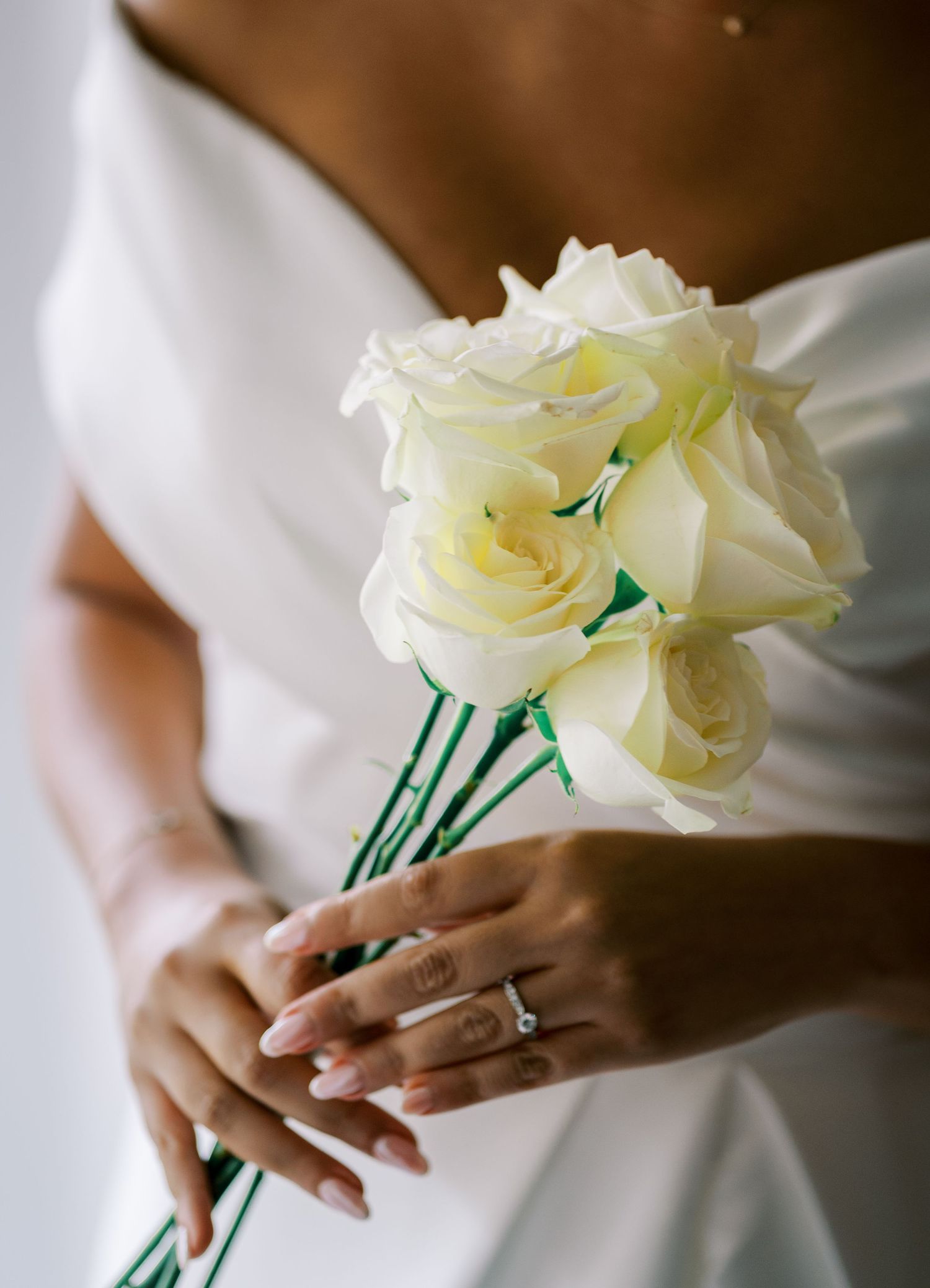 Close-up of white roses and delicate hands against white wedding dress fabric.