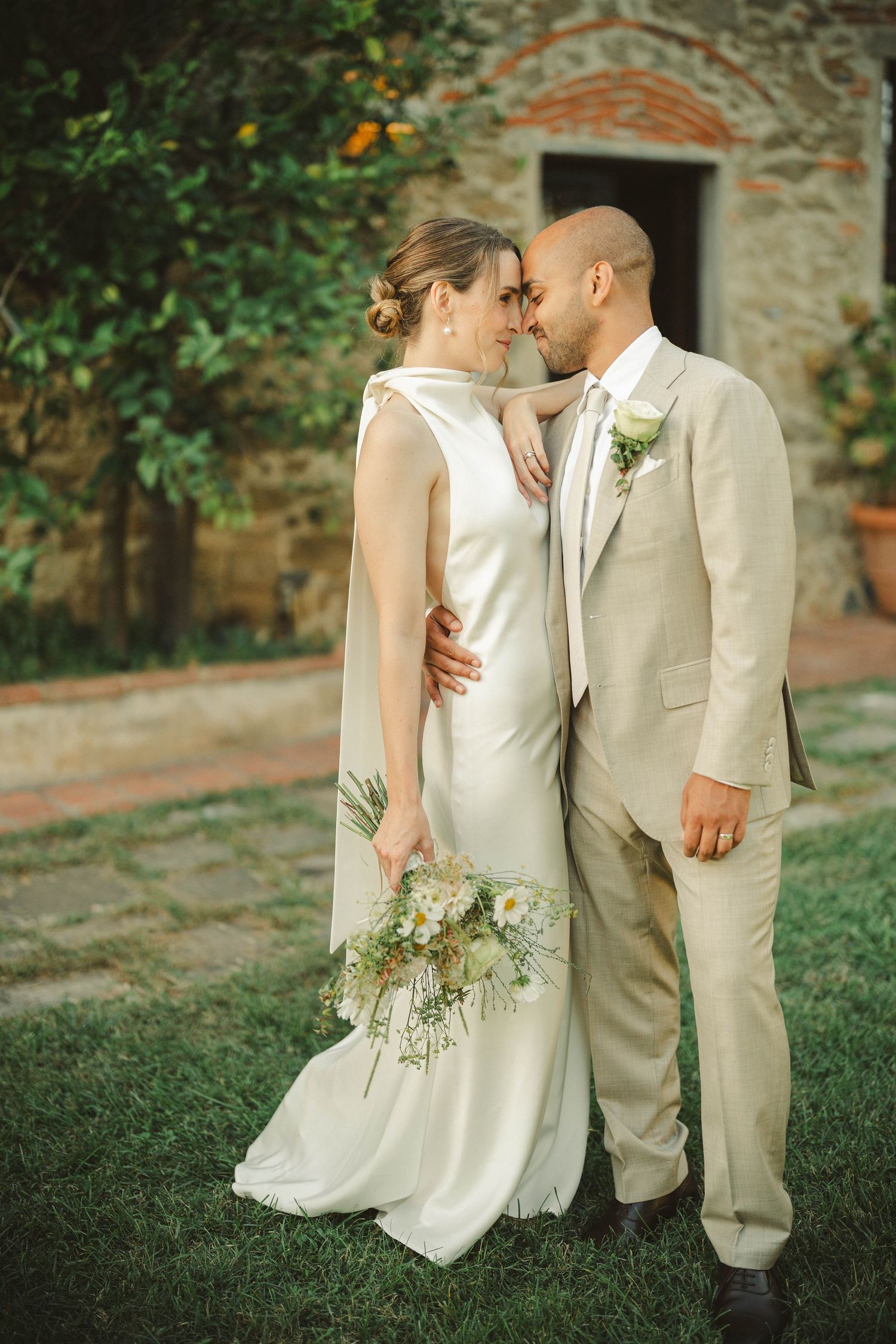 An intimate wedding portrait in front of a rustic stone building with delicate floral details.