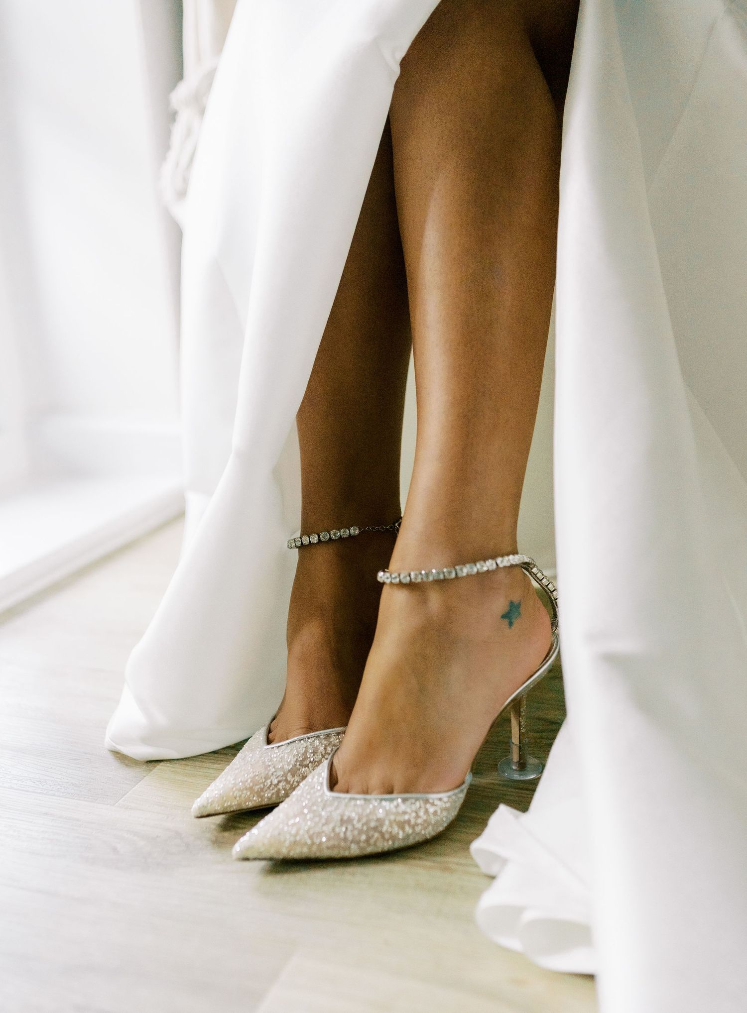Close-up of sparkly bridal shoes peeking beneath white wedding dress.
