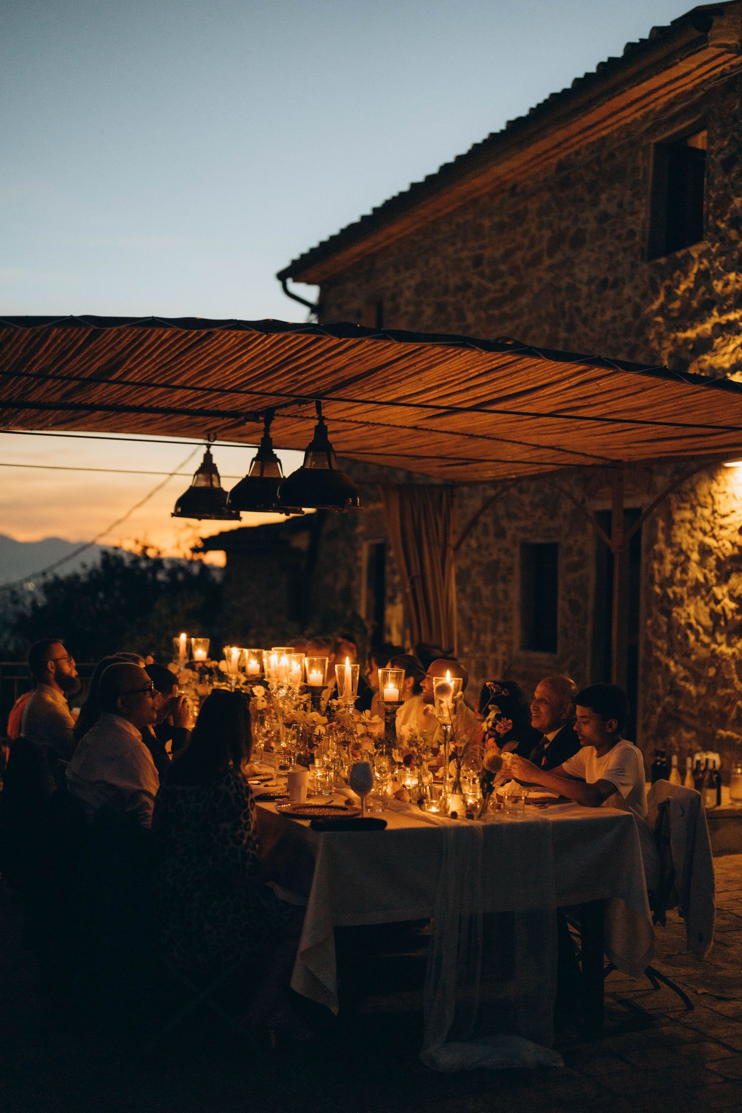Romantic sunset dinner reception under a rustic stone building with glowing ambient lighting.