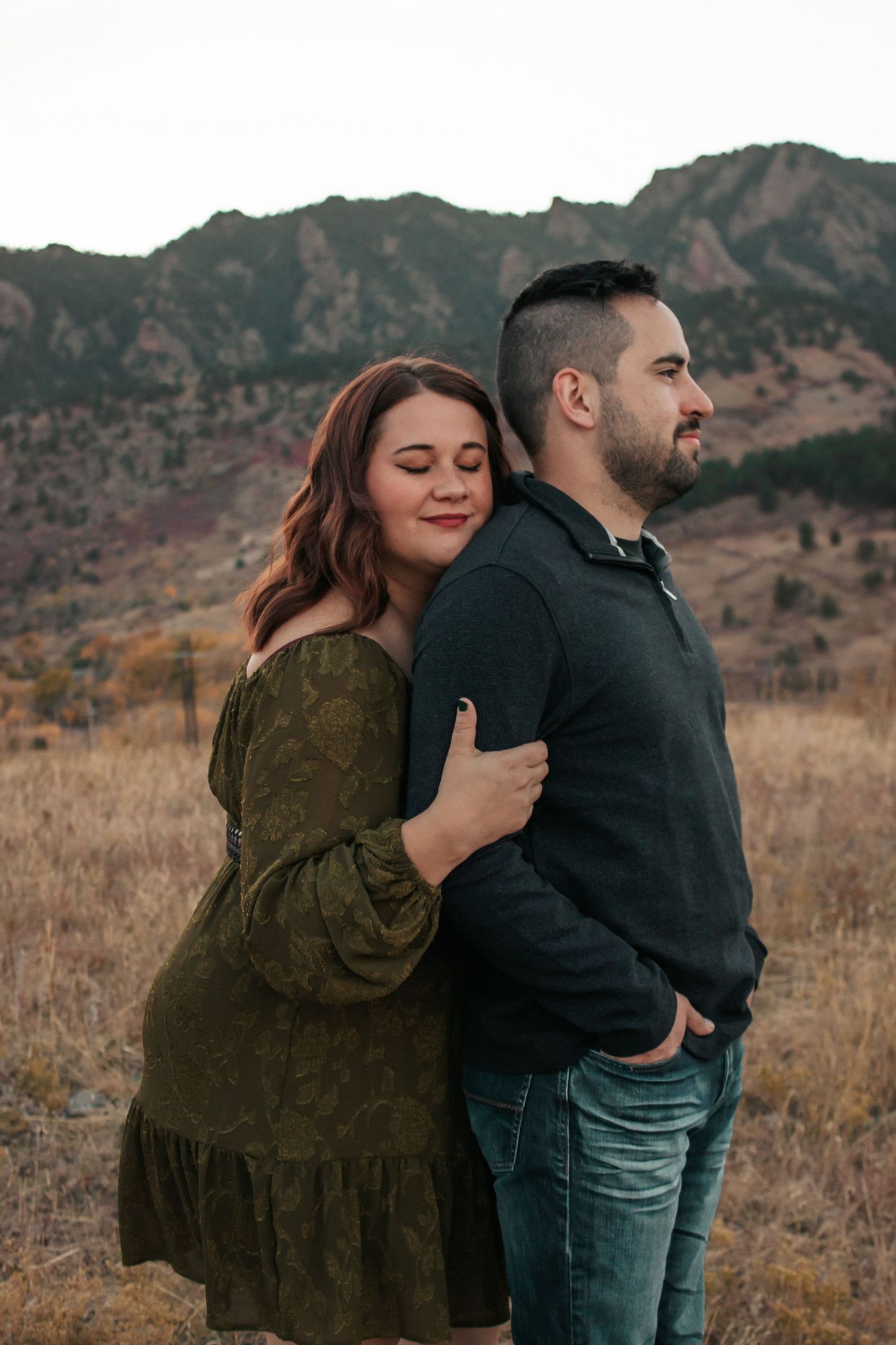 A romantic couple embraces in front of the Flatirons mountains near Boulder, Colorado during golden hour.