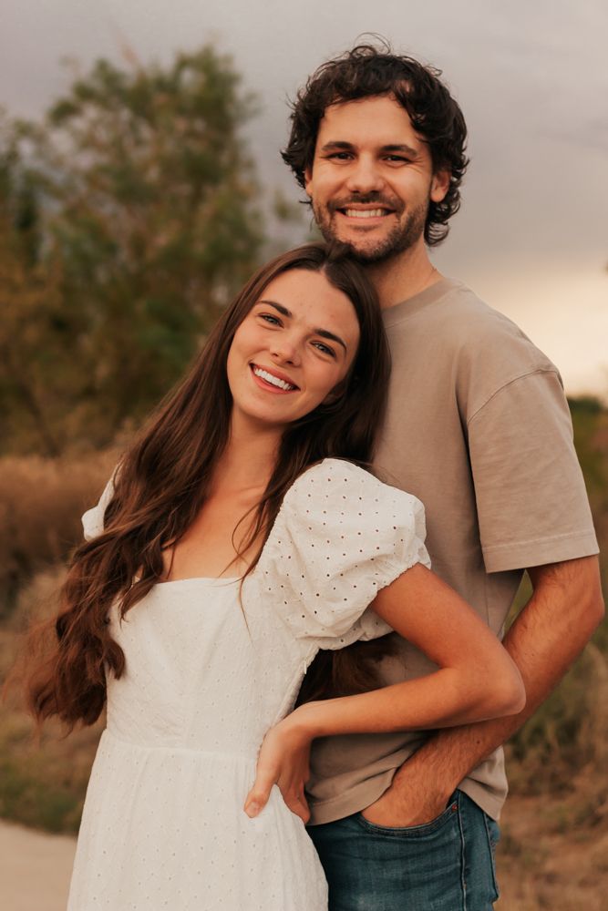 A couple embracing and laughing together during a sunset photoshoot in a natural outdoor setting.