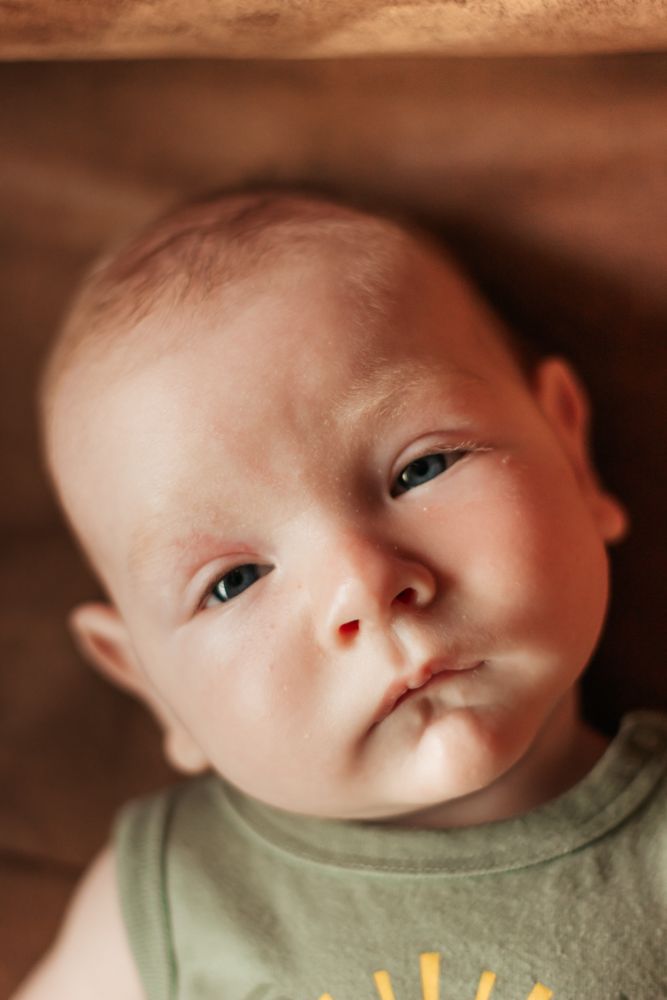 A baby wearing a green t-shirt looks up at the camera with a gentle expression | Westminster, CO motherhood & family photographer