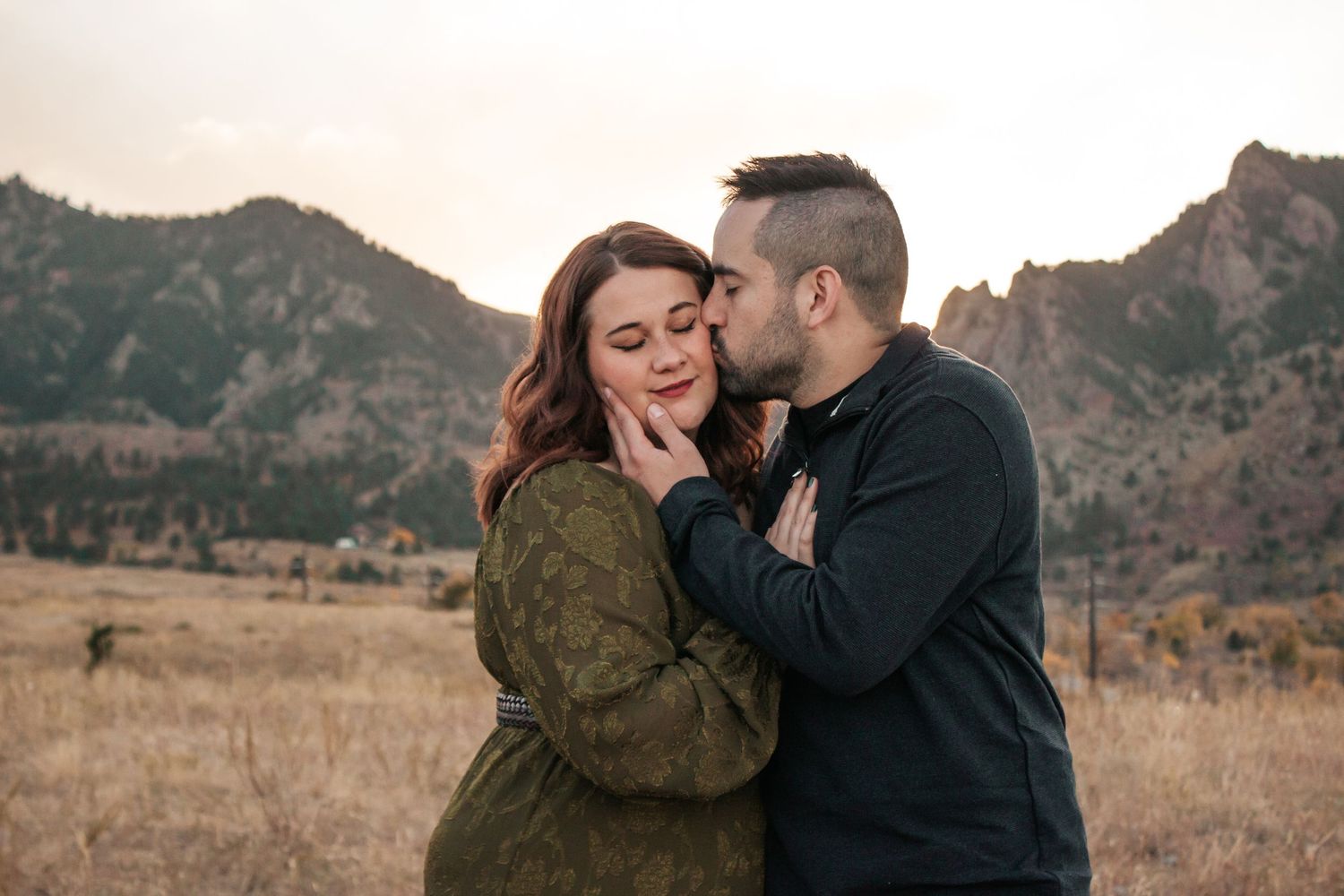 A couple shares romantic moments in a scenic mountain landscape during golden hour.
