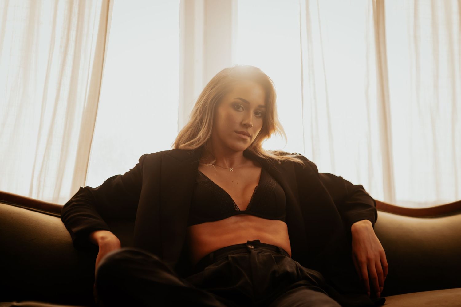 Woman in black outfit relaxing on sofa with dramatic backlit window glow.