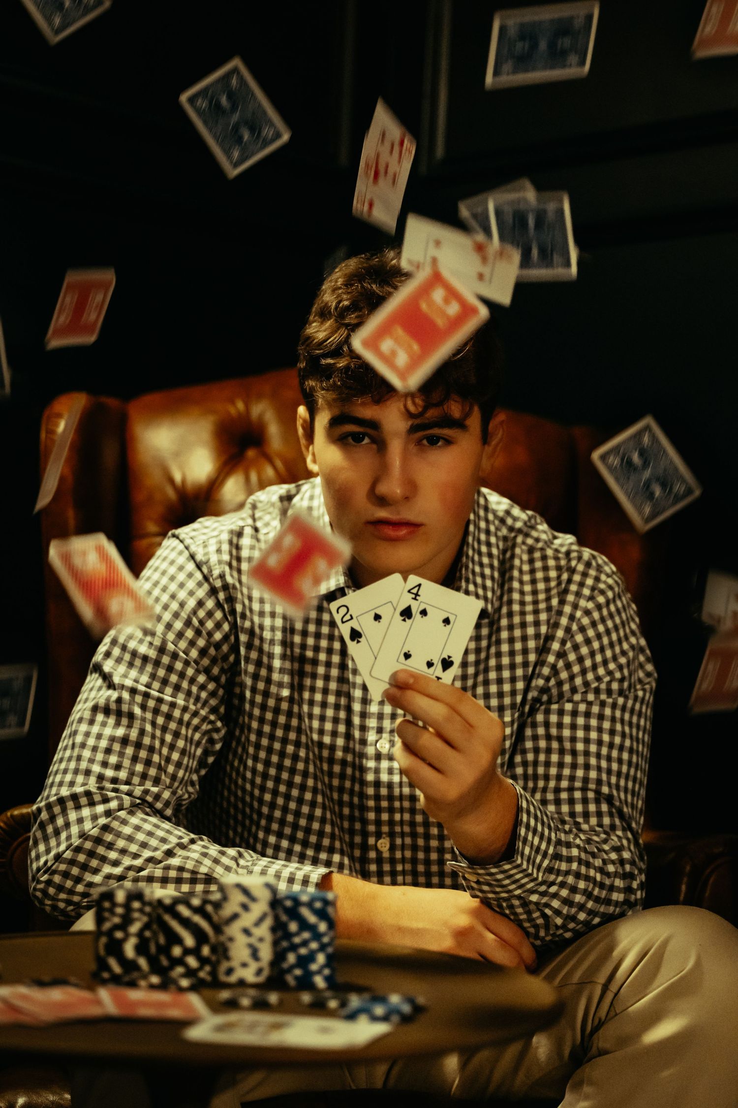 Teen boy holding playing cards with cards falling around him in dramatic poker scene.