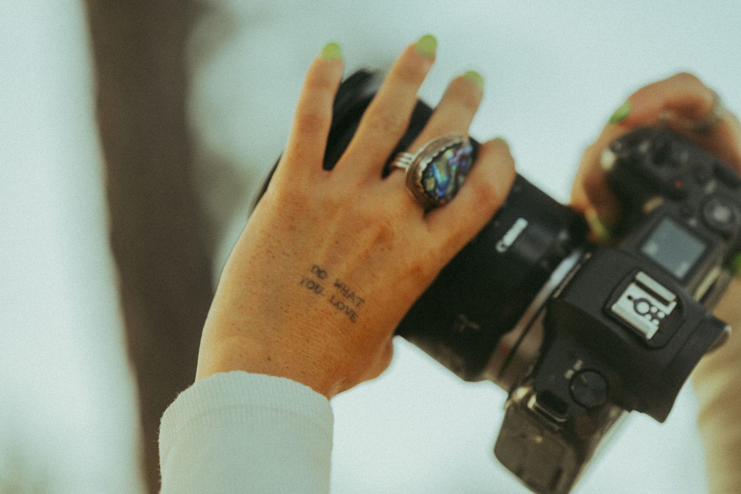 Close-up of tattooed hand holding vintage film camera with colorful ring.