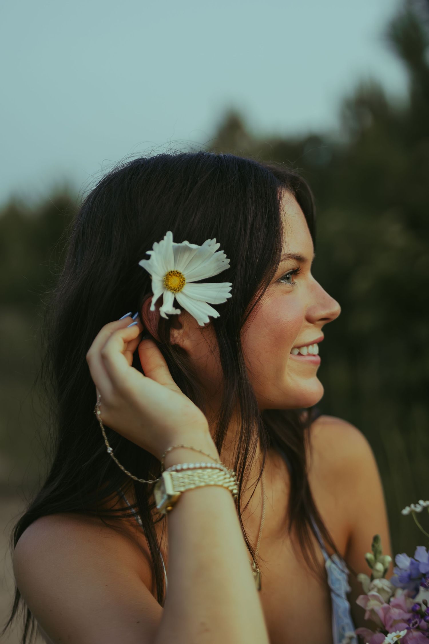 Smiling young woman with daisy flower tucked behind ear in soft evening light.