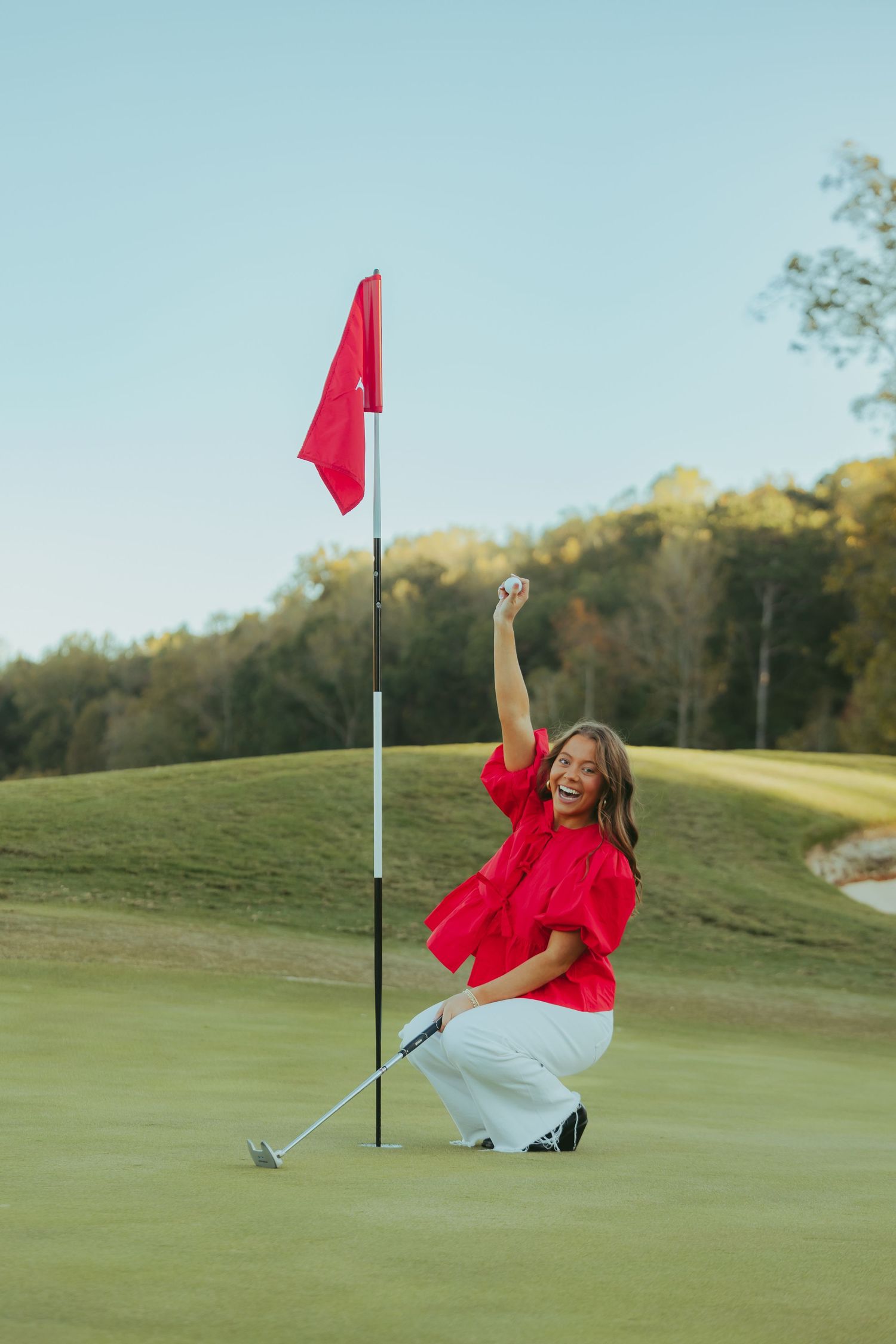 Excited woman in red top celebrates a hole-in-one on a golf course green with red flag. golf senior photos.