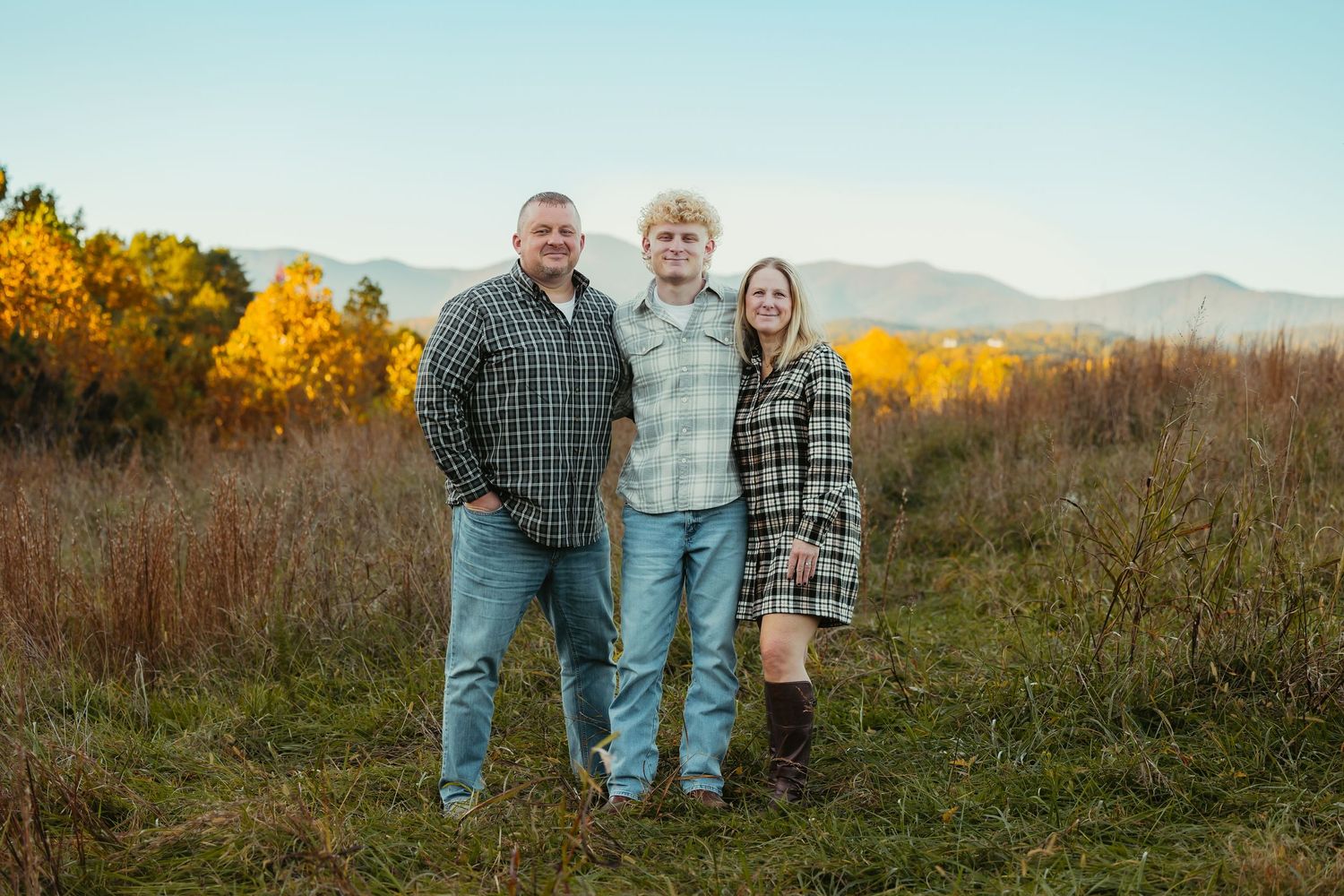 family smiles together in an autumn field with colorful foliage and mountains in background.