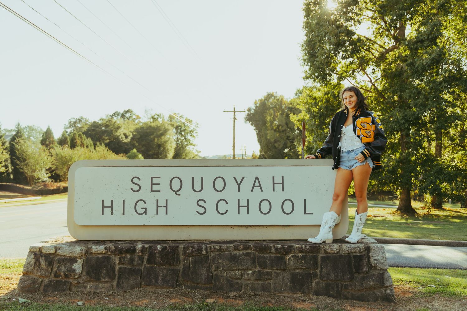 Teen girl posing on Sequoyah High School entrance sign in sunny outdoor setting.