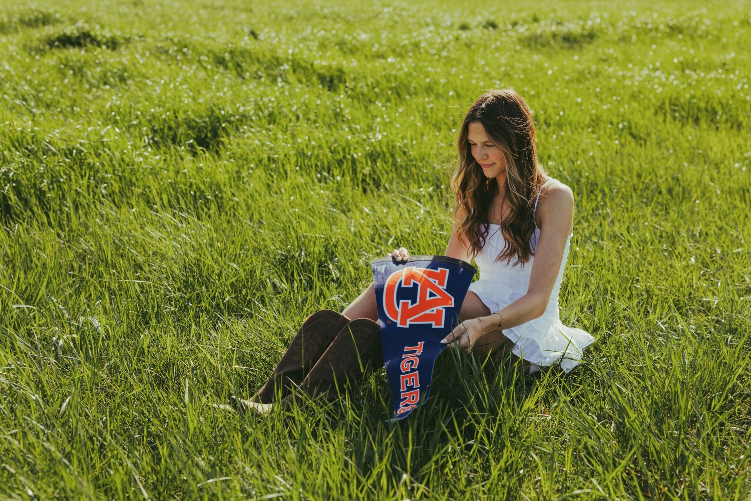 white graduation dress sitting in green grass holding Auburn University jersey.
