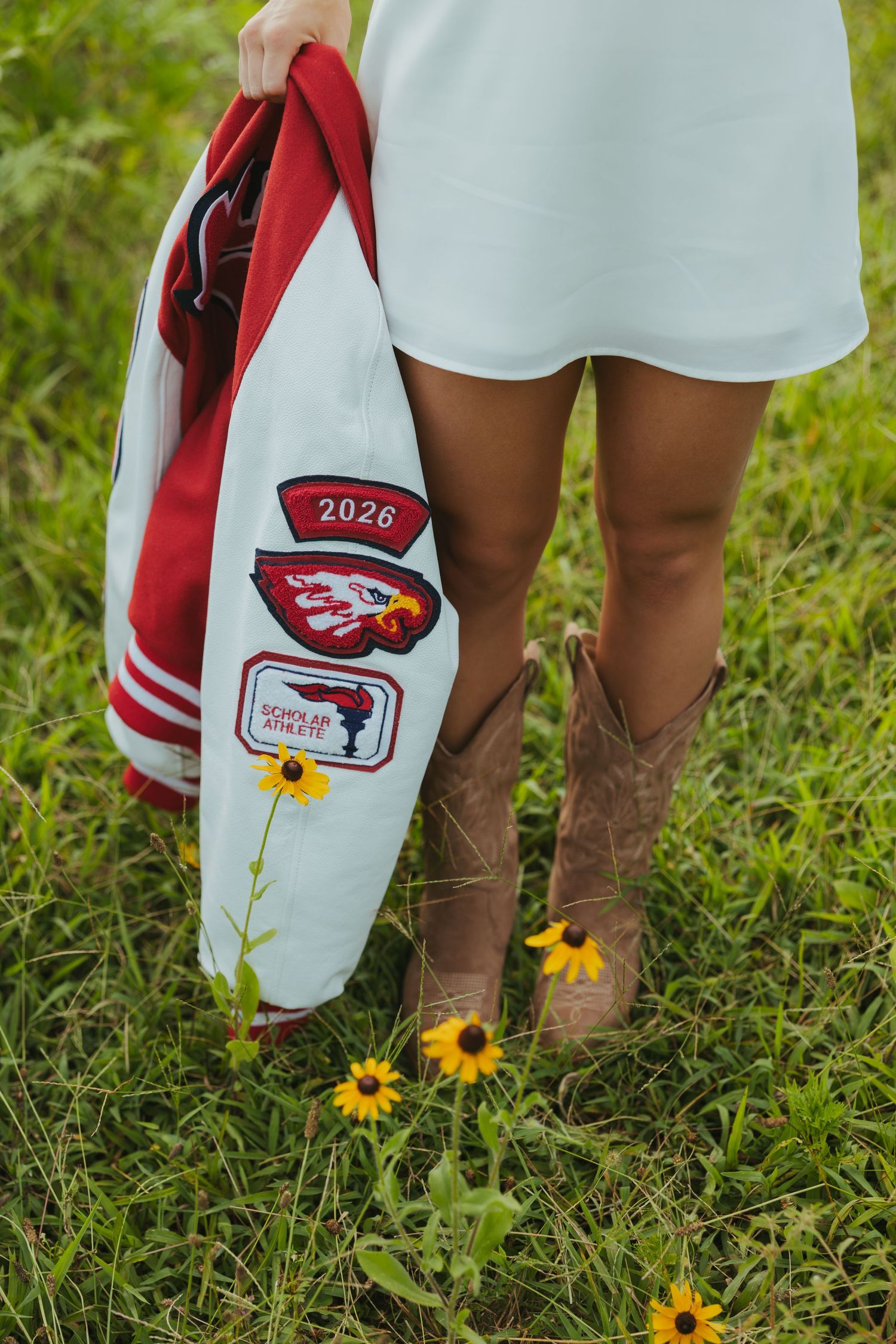 Close-up of student holding red and white letterman jacket with 2026 patch in flower field.