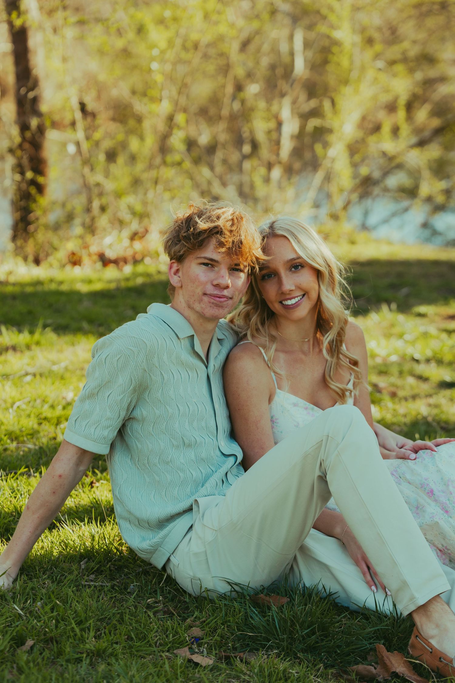 Smiling young couple sitting together on grass in sunny outdoor park setting.
