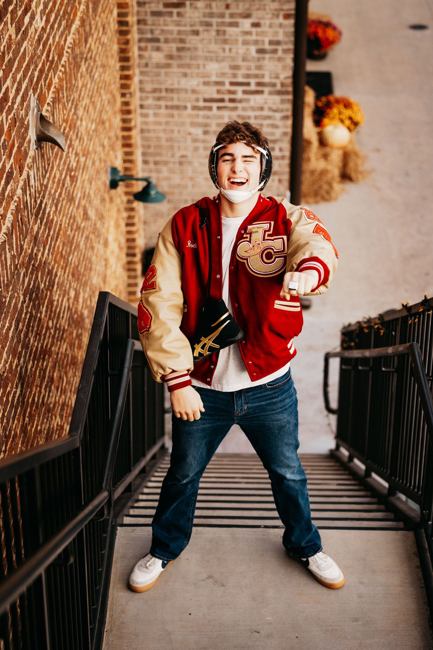 Laughing teen boy in red letterman jacket and headphones posing on metal staircase.