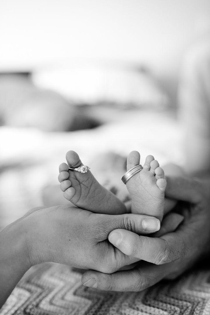 Black and white photo of a newborns feet in its parents hands and with wedding rings on its toes - Kelly Chapman Photographer Perth