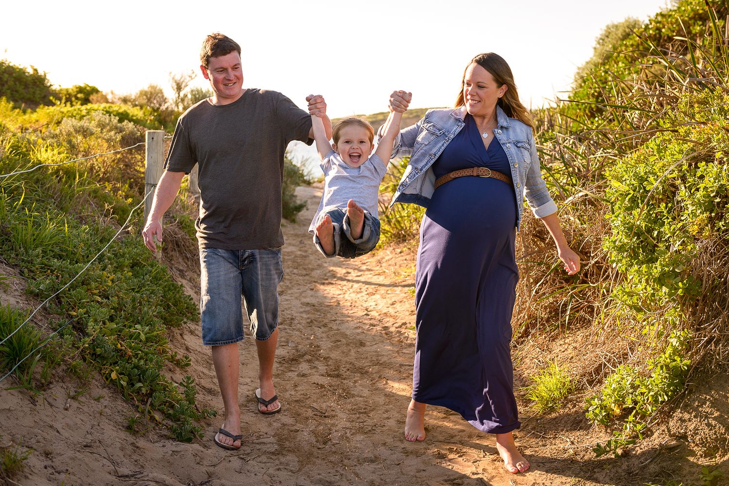 Maternity photo of young couple walking hand in hand with young son and lifting him up - Kelly Chapman Photographer Perth