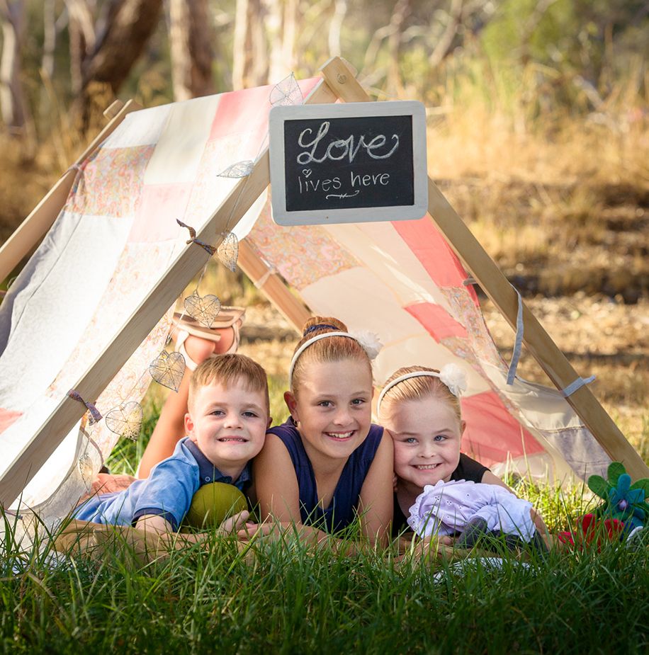 Photo of 3 young siblings under a tent with sign saying Love lives Here - Kelly Chapman Photographer Perth