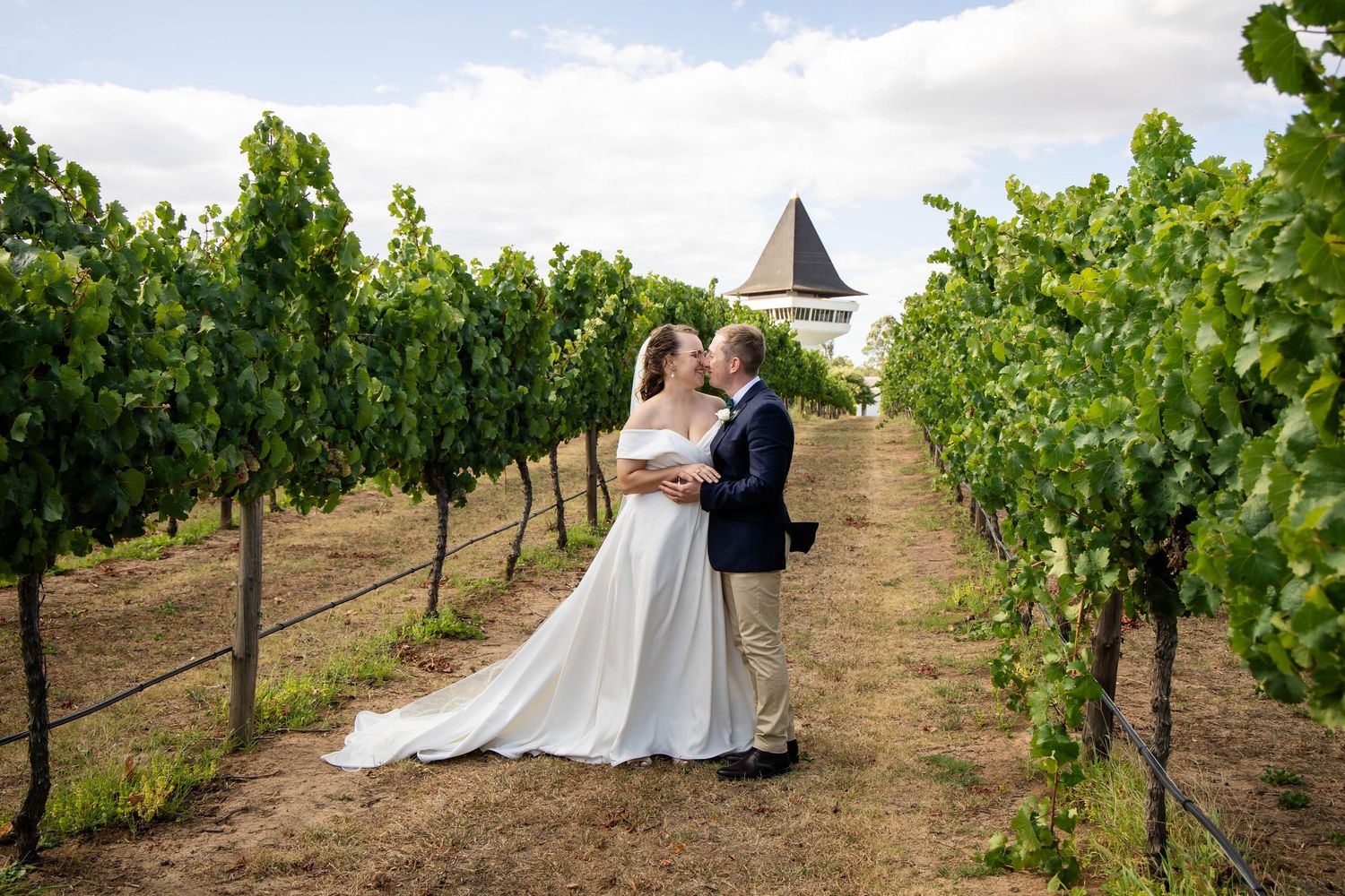 Newlyweds pose together among sunny vineyard rows during their wedding photoshoot at a scenic winery.