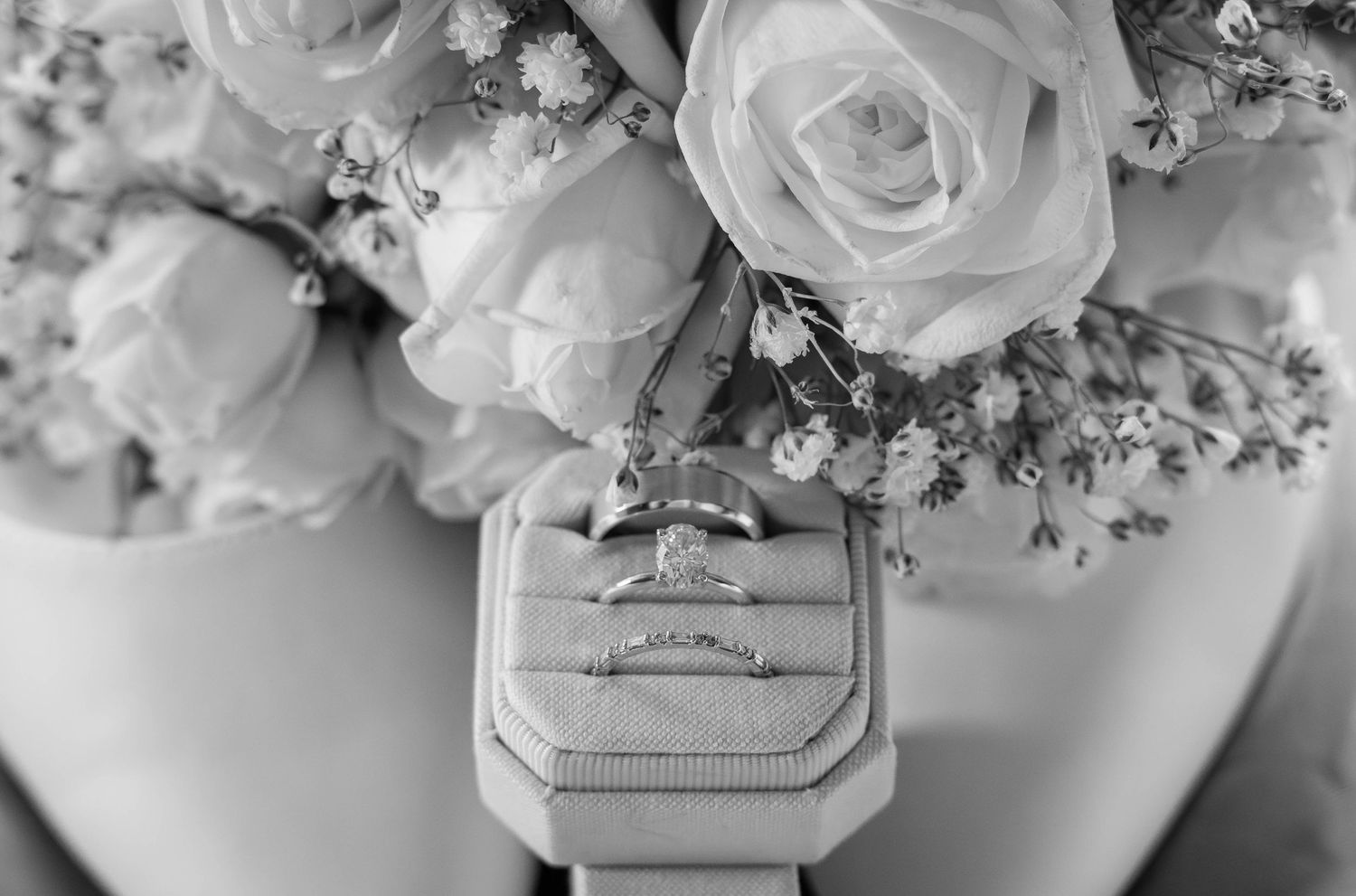 Overhead view of decorative wedding ring box and pastel pink roses with baby's breath floral arrangement in black and white.