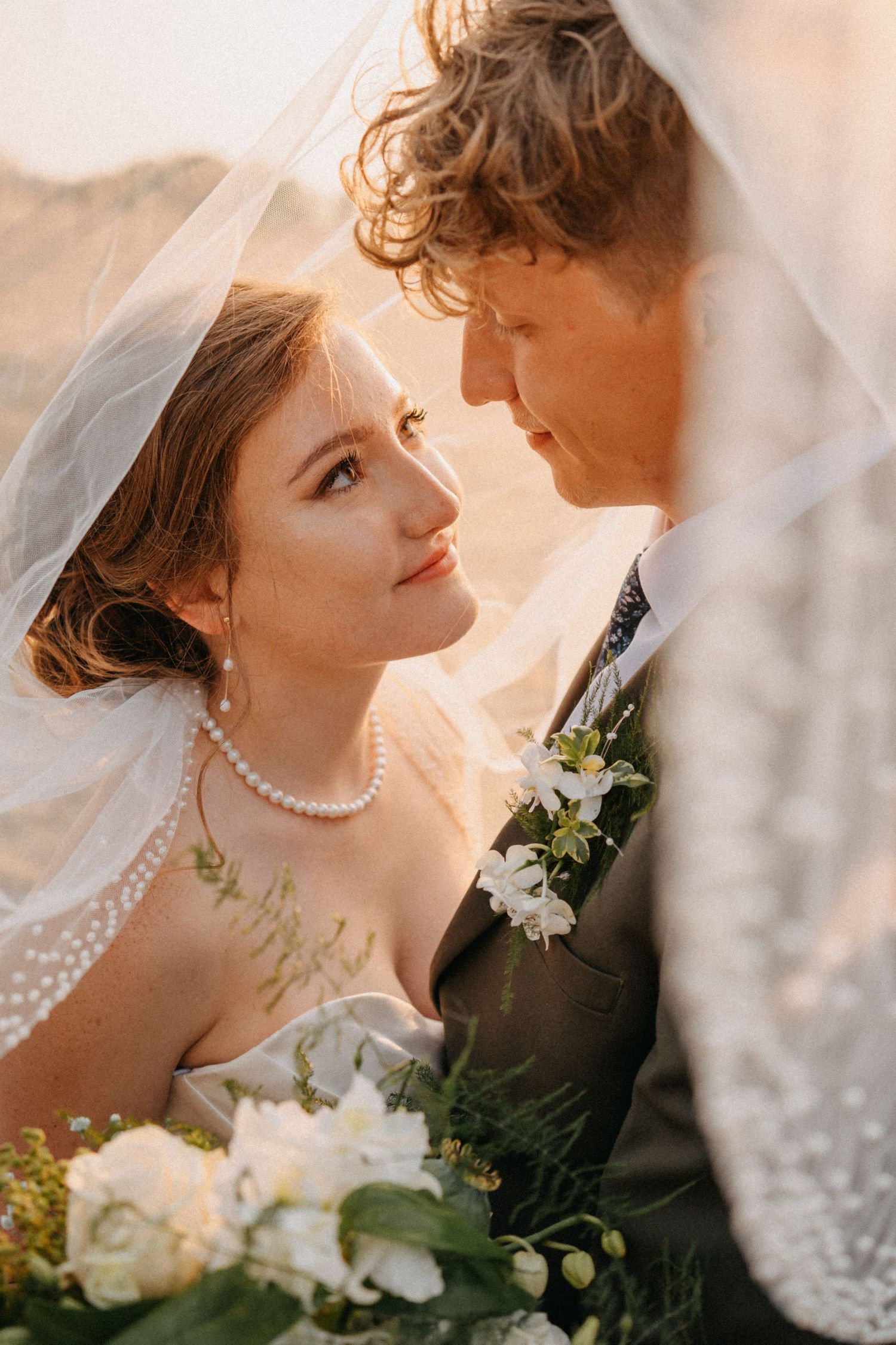 Romantic wedding portrait with bride in pearl necklace and veil holding white bouquet during golden hour.