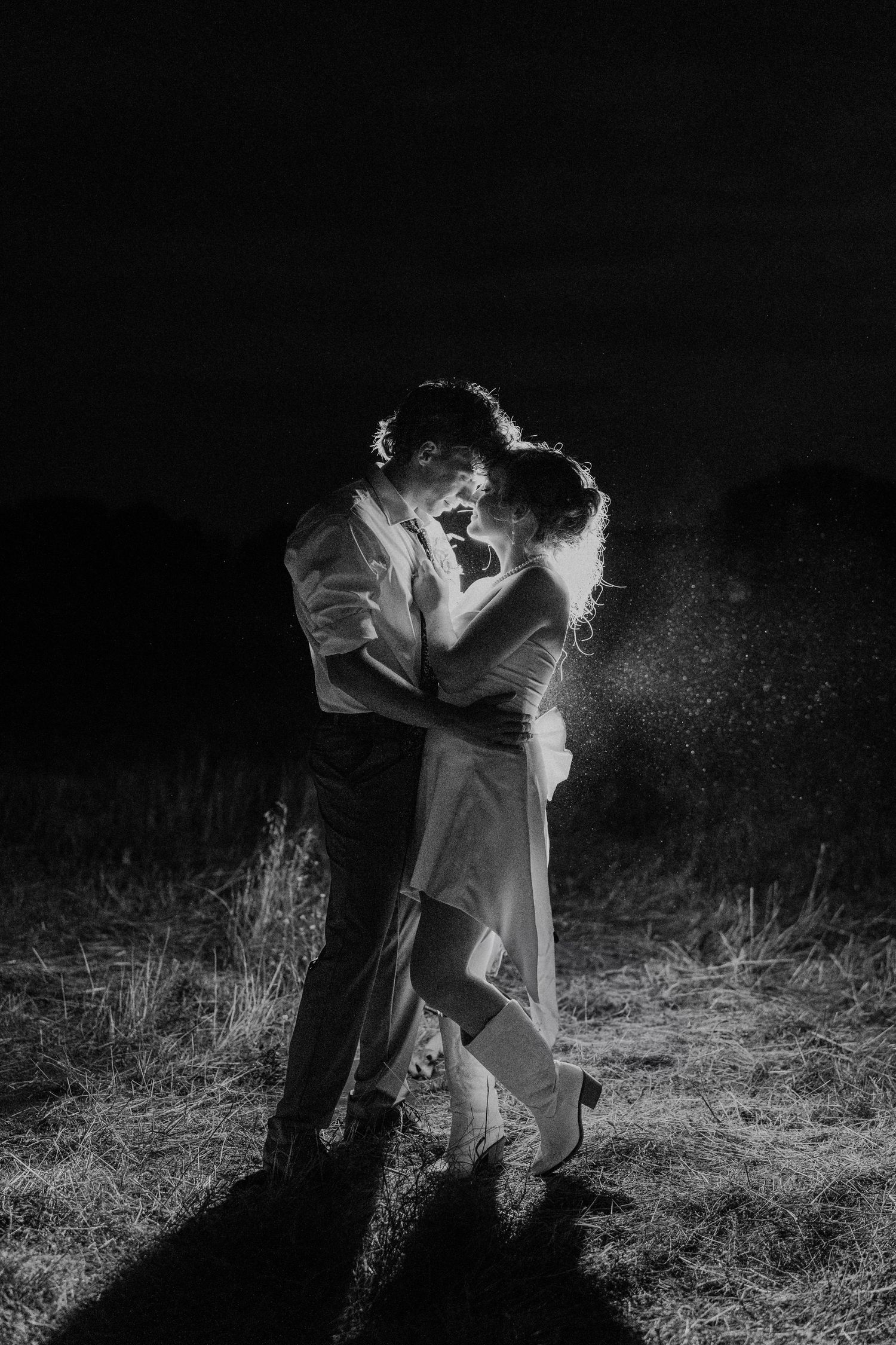 A couple in white clothing dances together in a dramatic black and white photo series with flour creating ethereal effects.