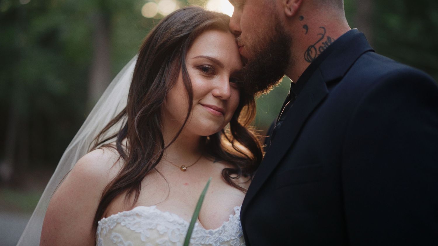 A couple shares a romantic moment outdoors with natural greenery in the background.