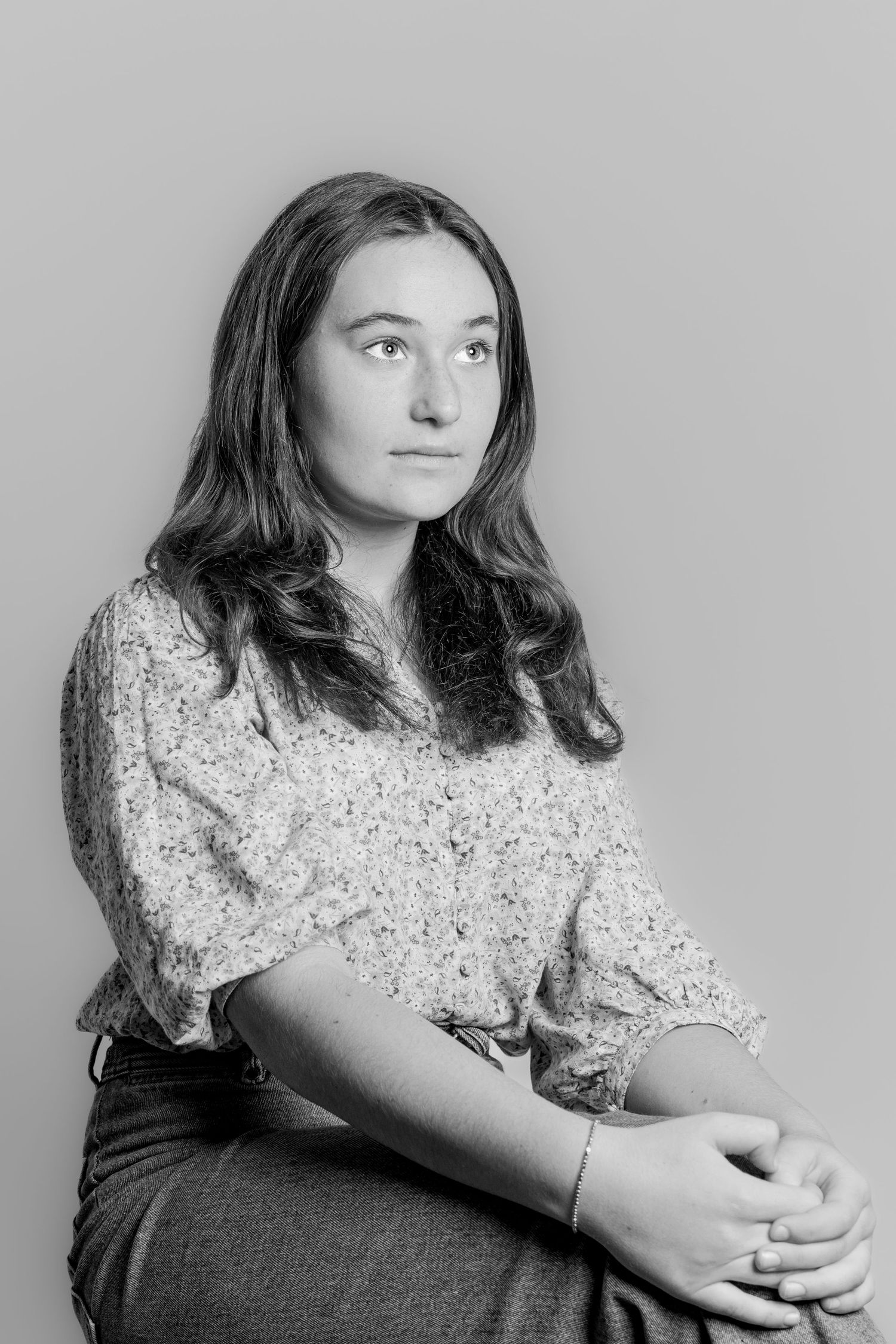 Black and white portrait of a teenage girl with long brown hair, sitting and gazing thoughtfully.
