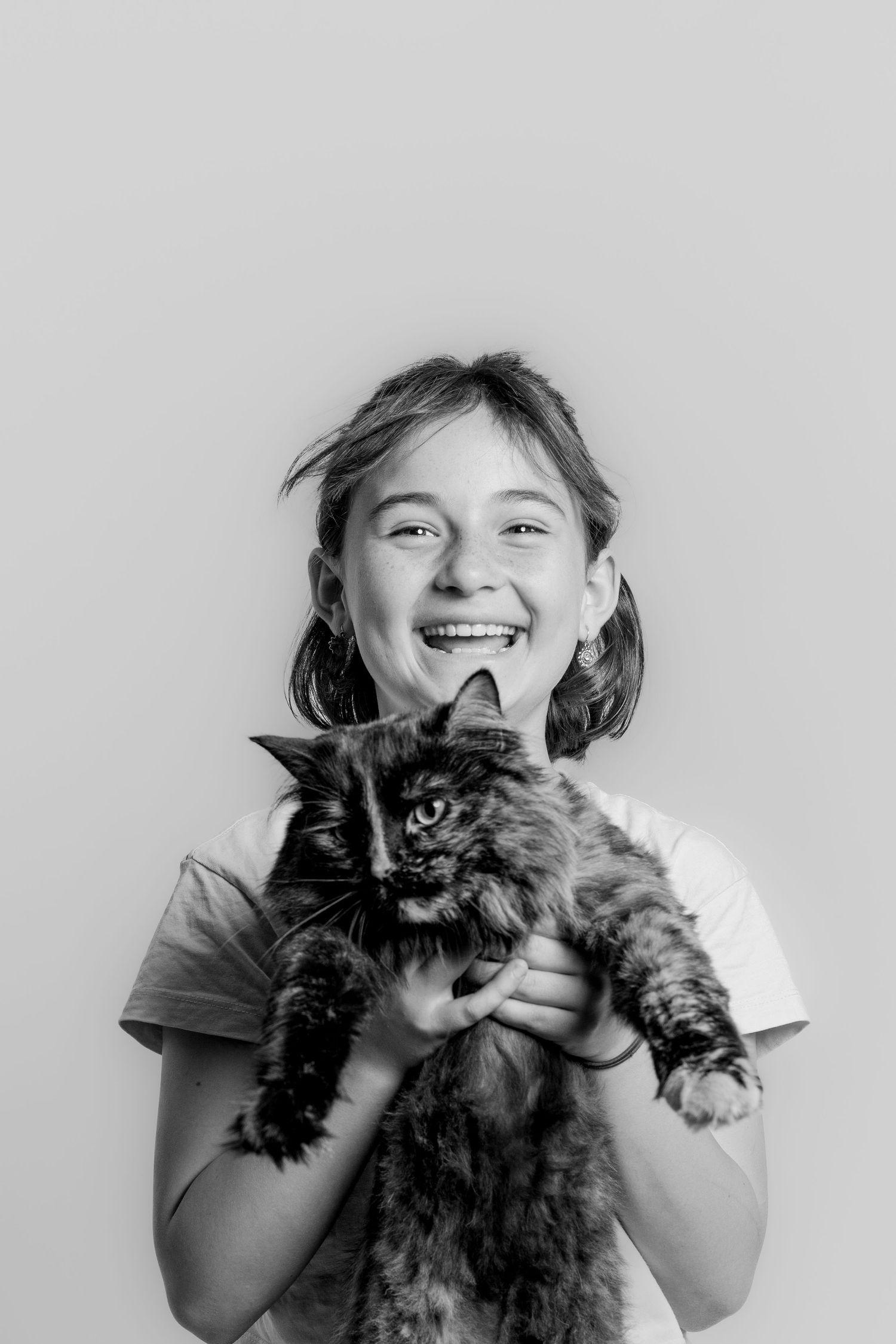 A laughing girl holds a fluffy black cat in a black and white studio portrait.