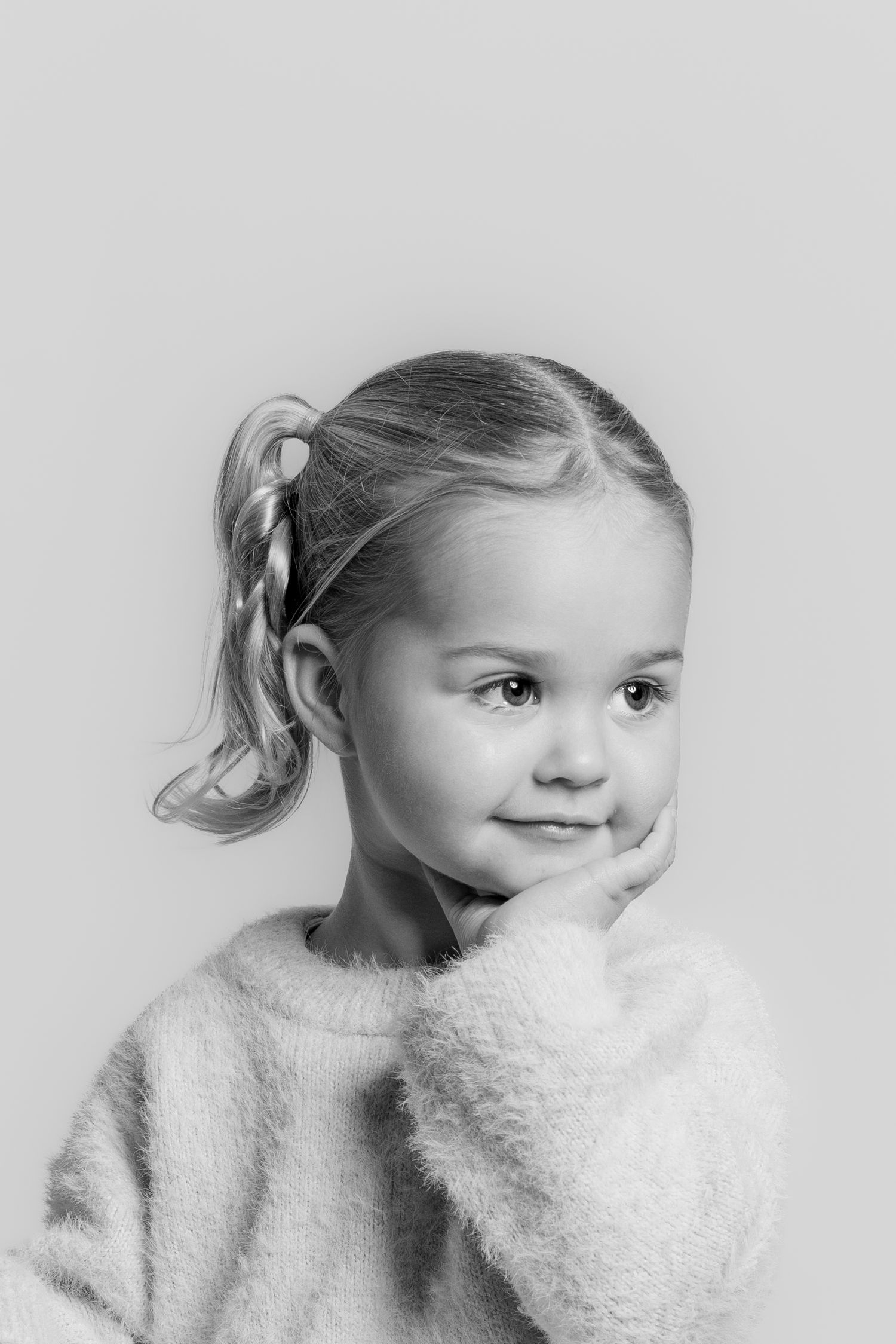 Black and white portrait of a young girl with a braided ponytail, resting her hand on her cheek.