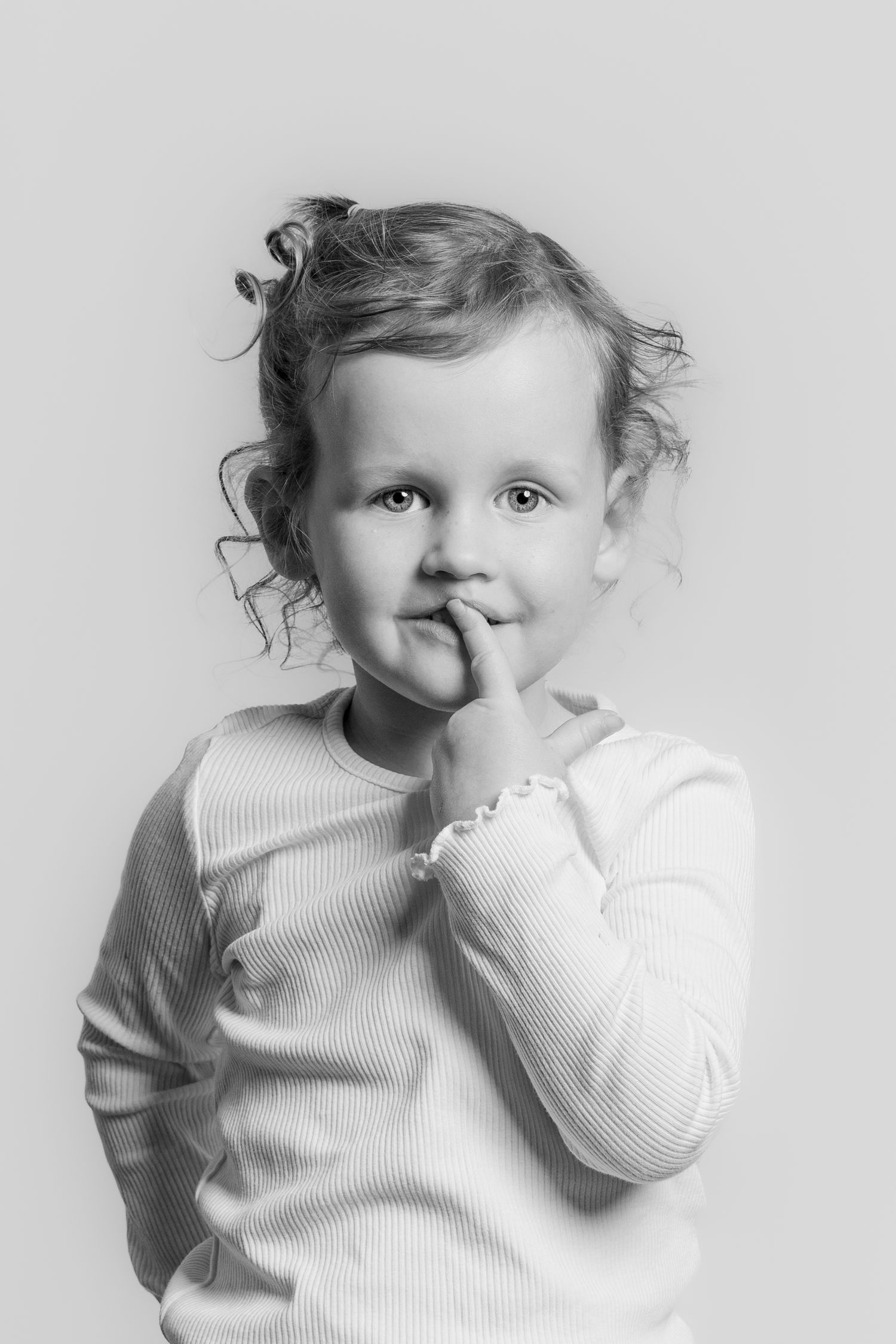 Black and white portrait of a cute toddler girl with curly hair, finger on her lips.