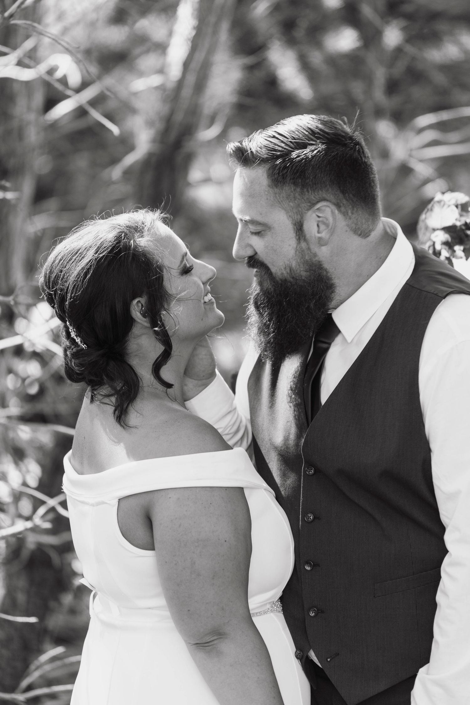 Black and white wedding portrait of bride and groom gazing at each other outdoors.