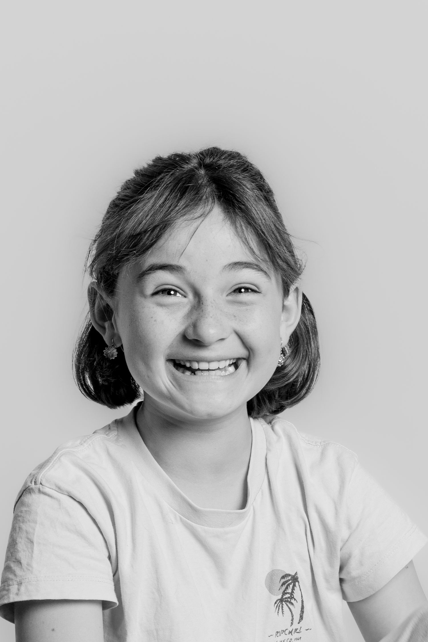 A cheerful young girl smiles broadly in a black and white studio portrait.
