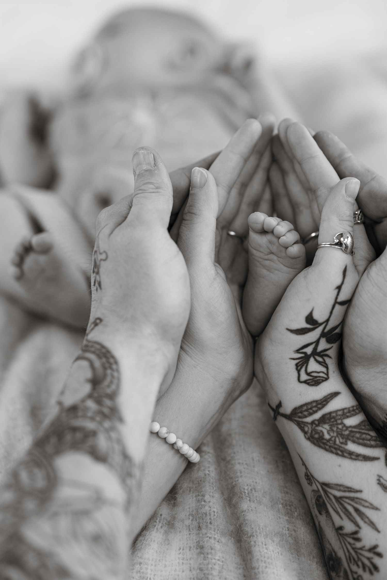 Black and white photo of tattooed parents cradling newborn baby feet in their hands.