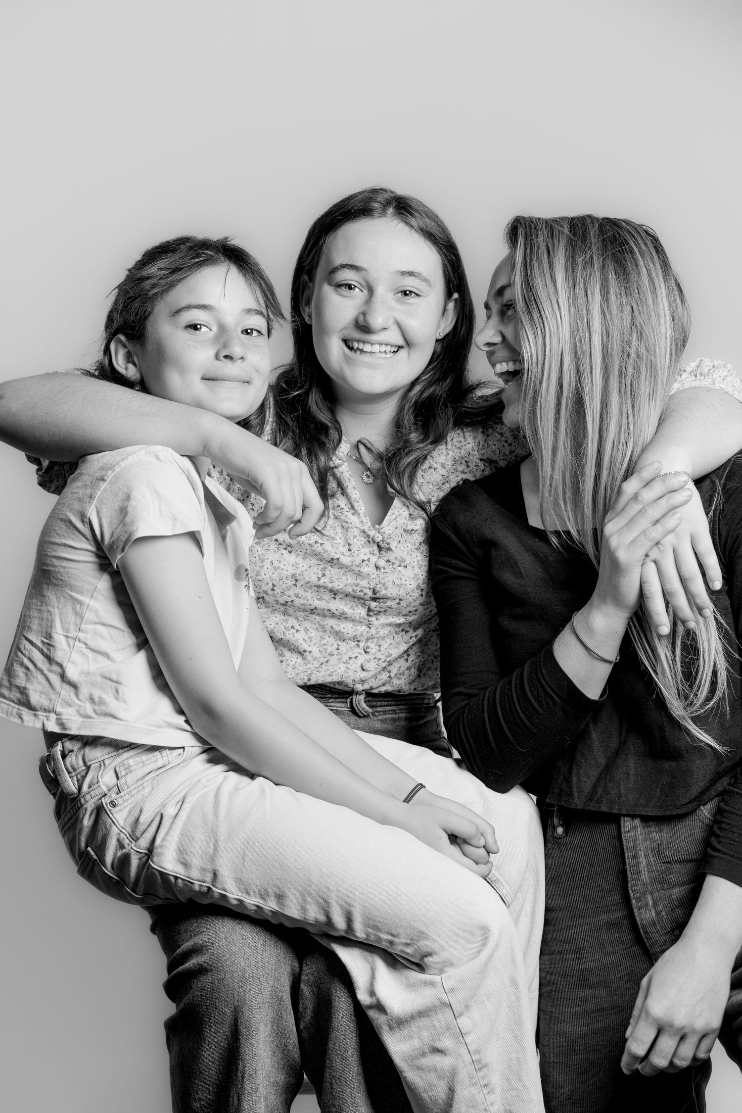 Black and white studio portrait of three young women smiling and embracing together.