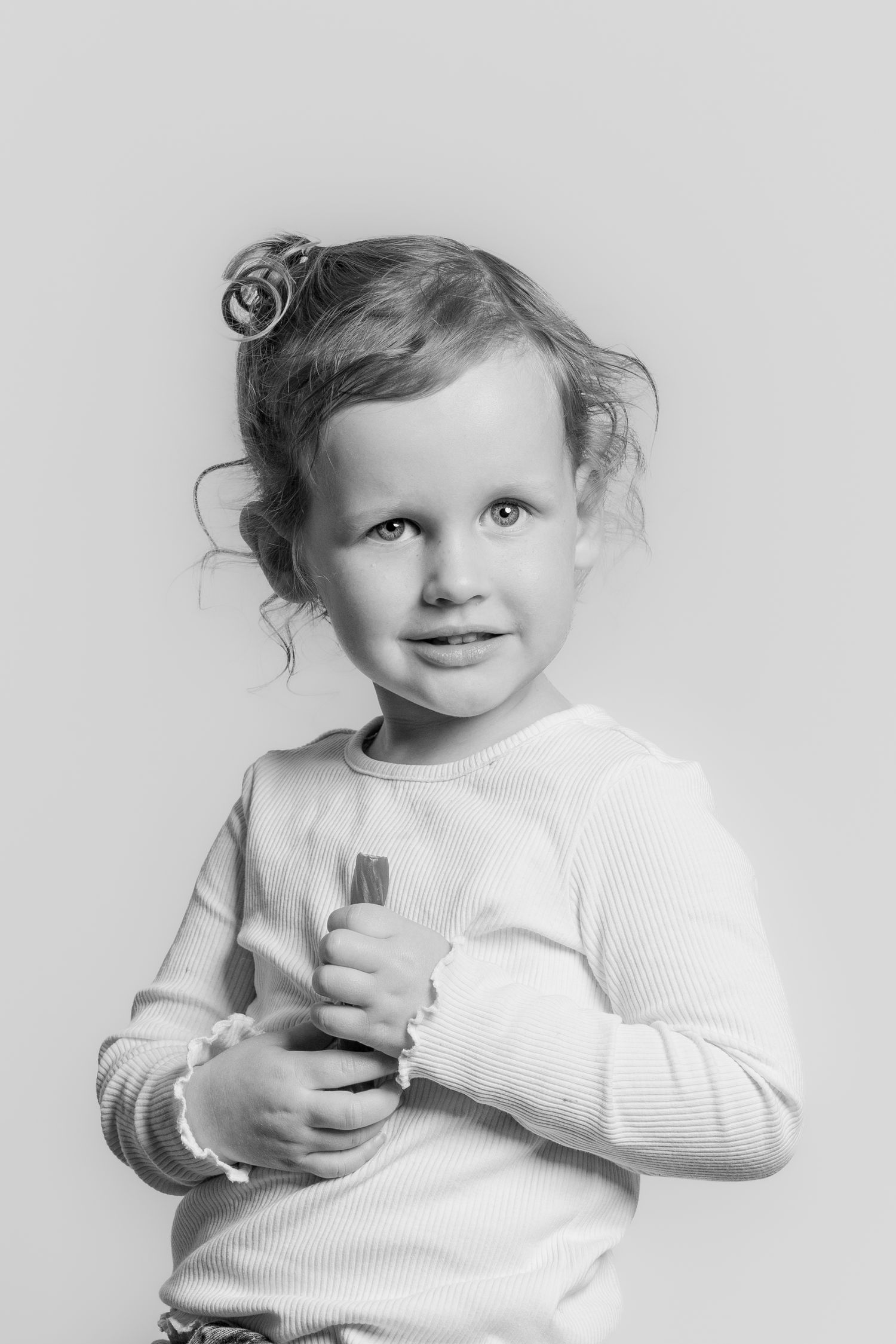 Black and white portrait of a young curly-haired girl in a white ribbed long-sleeve shirt.
