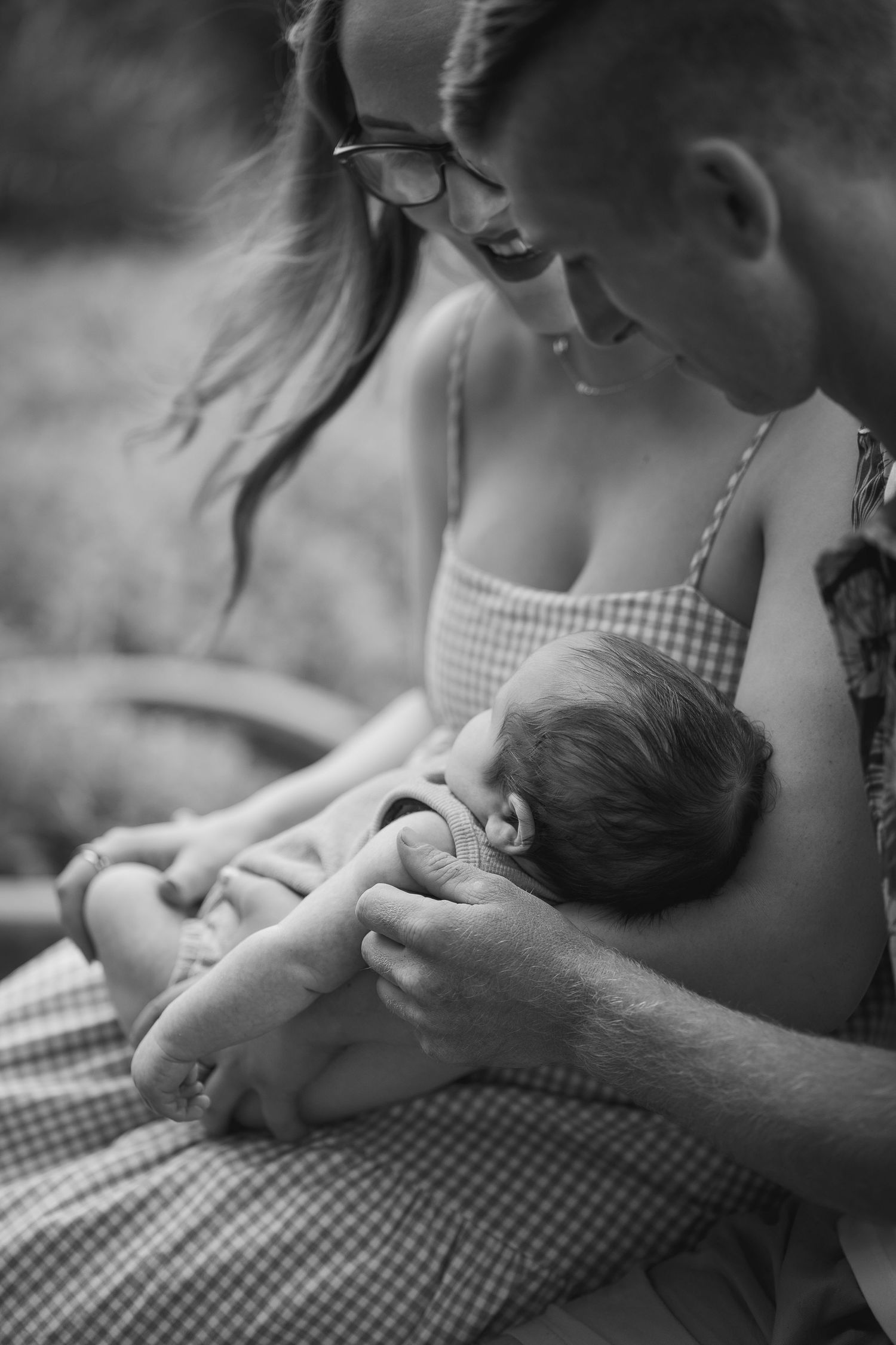 Black and white image of parents cradling their newborn baby together outdoors.