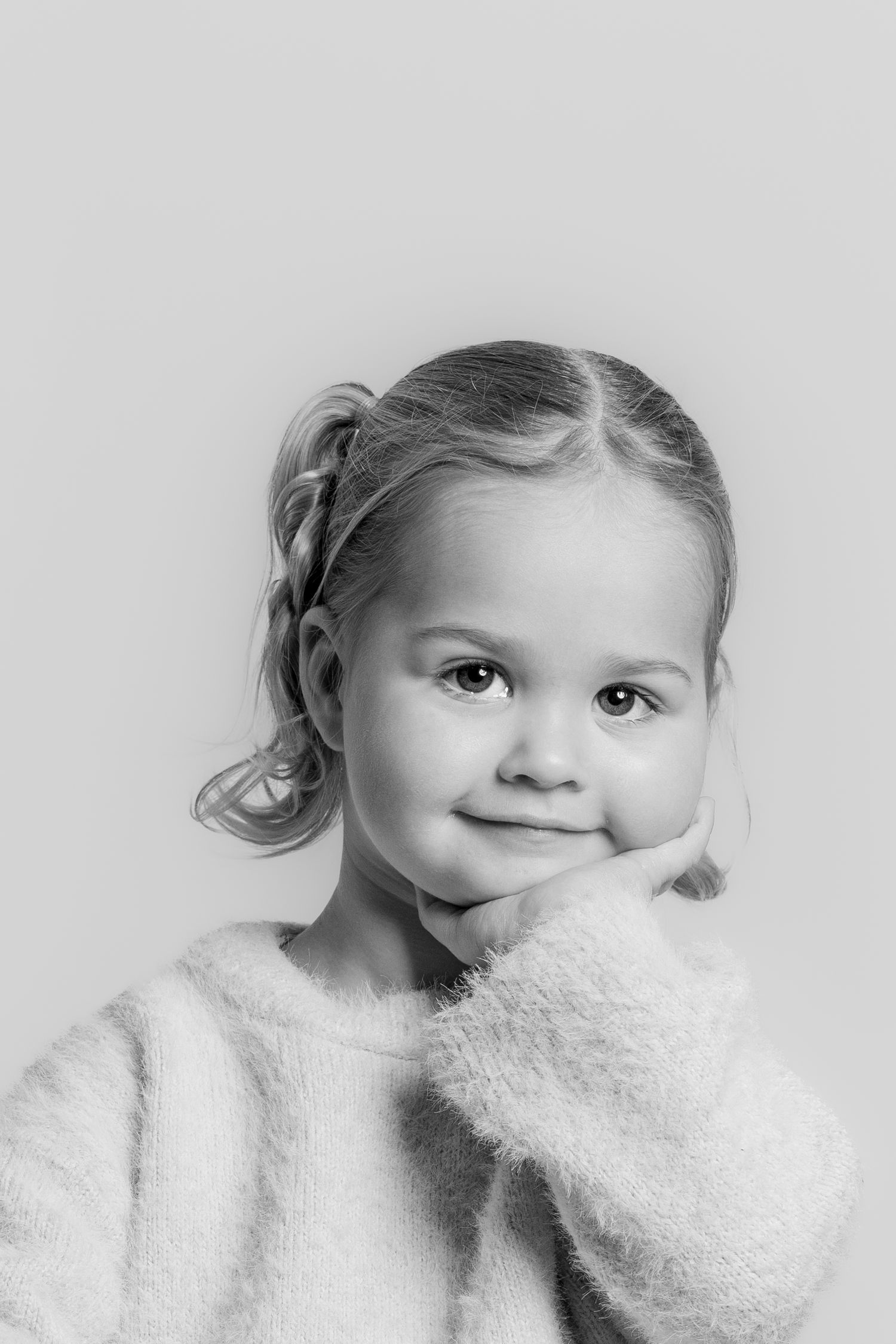 Black and white close-up portrait of a young girl resting her chin on her hand, smiling softly.