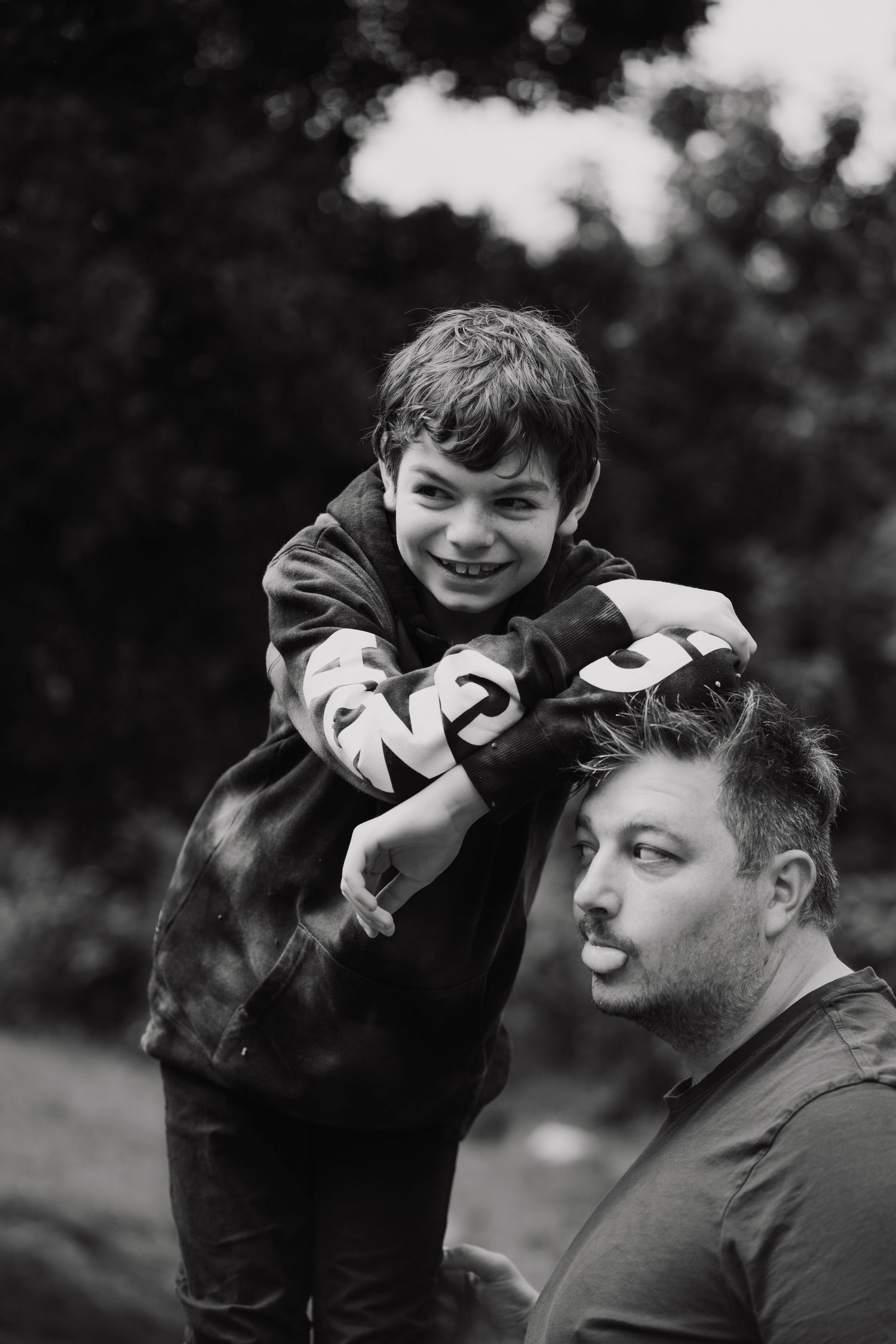 Black and white portrait of a smiling boy sitting on a mans shoulders outdoors in a park.