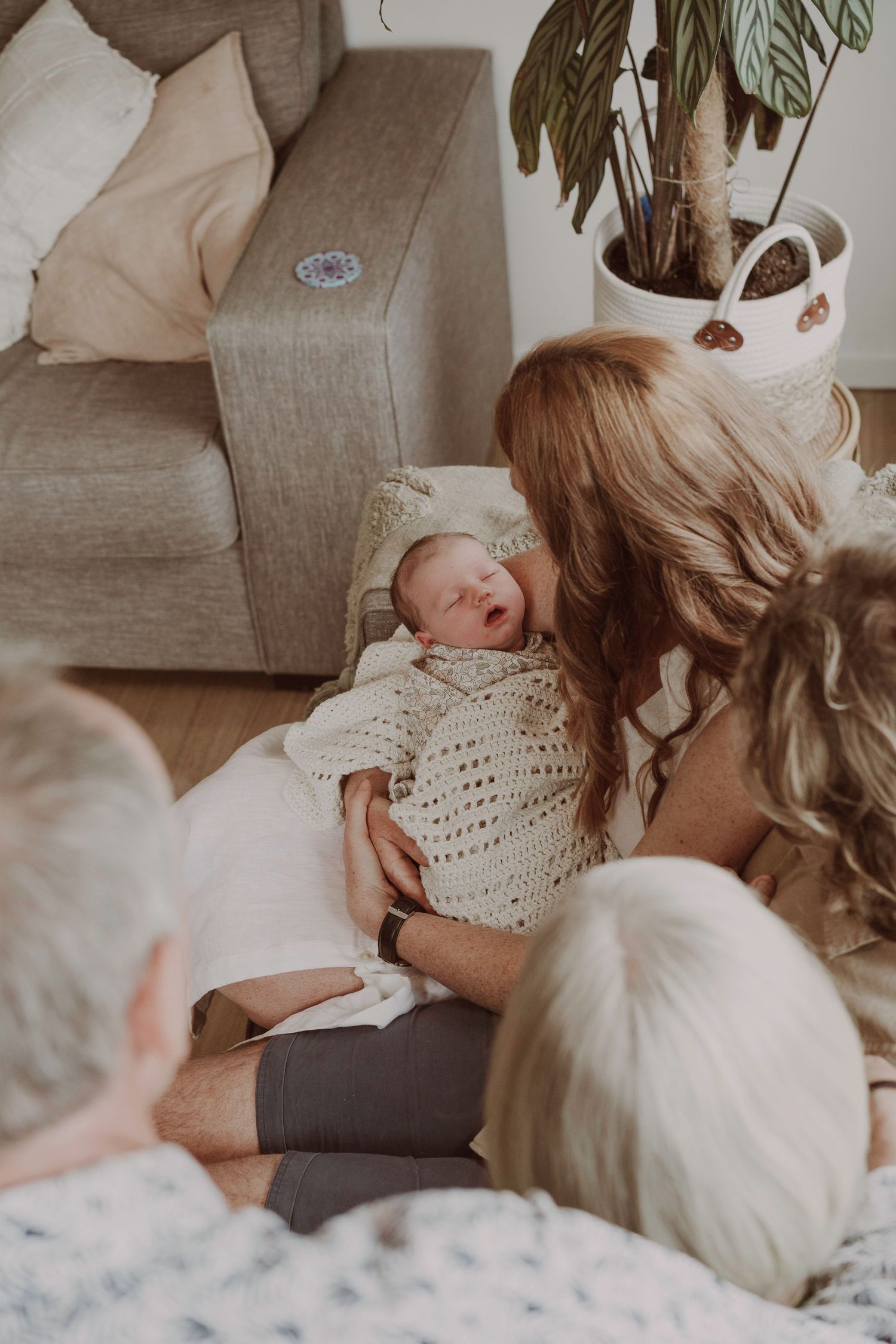 Red-haired mother gazes lovingly at her sleeping newborn baby wrapped in a cream knit blanket.