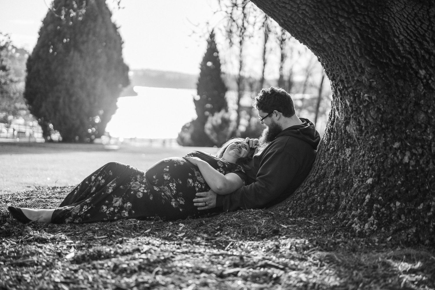 Couple relaxing under a large tree by the water, black and white maternity photography.
