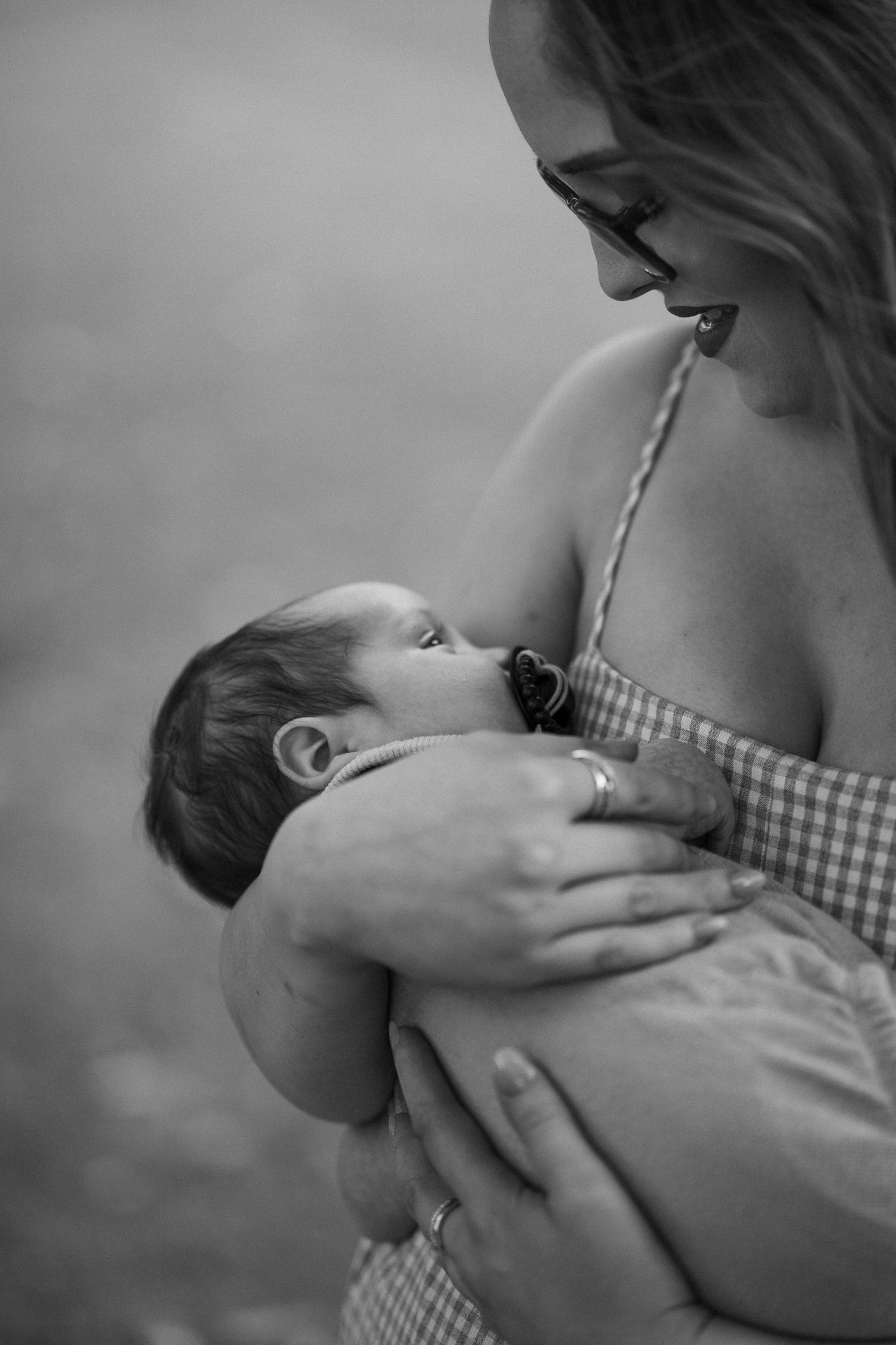 Black and white photo of a mother breastfeeding her newborn baby outdoors.